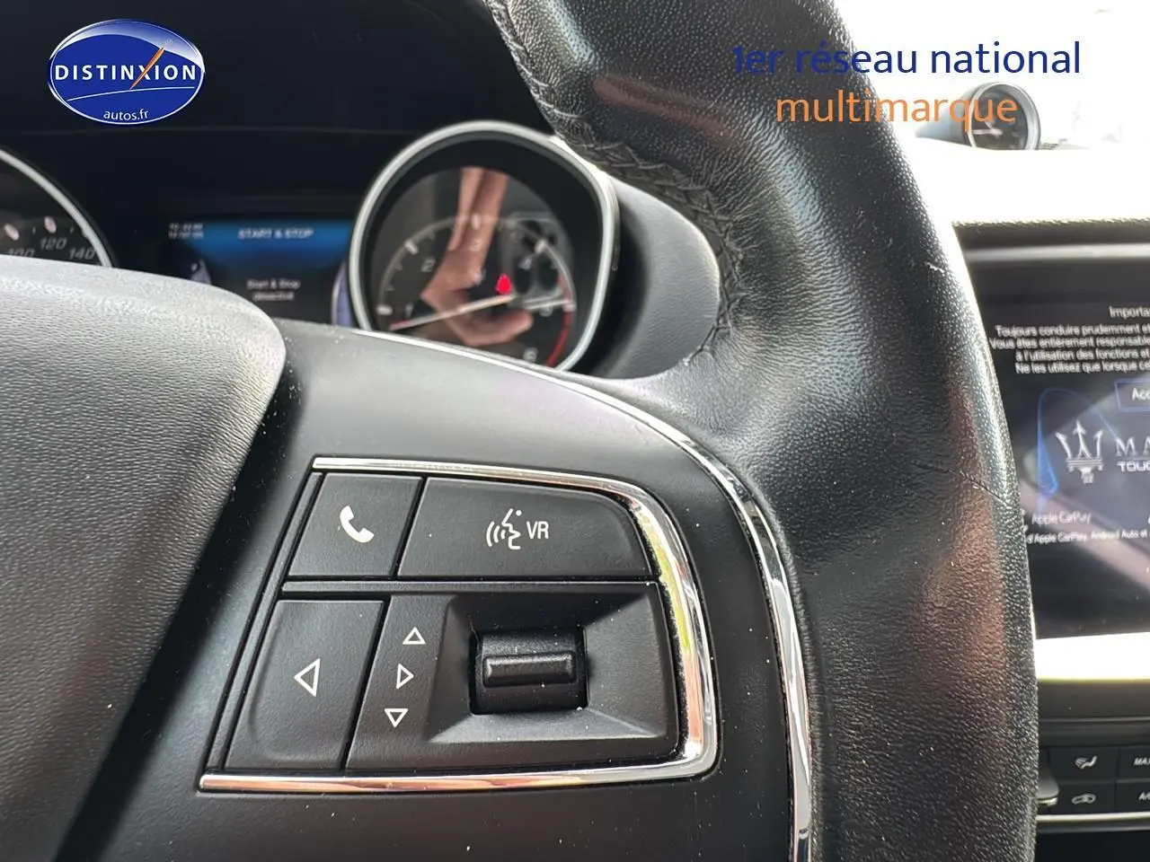 Gros plan sur les commandes au volant cuir noir du Maserati Levante gris, avec écran tactile visible en arrière-plan.