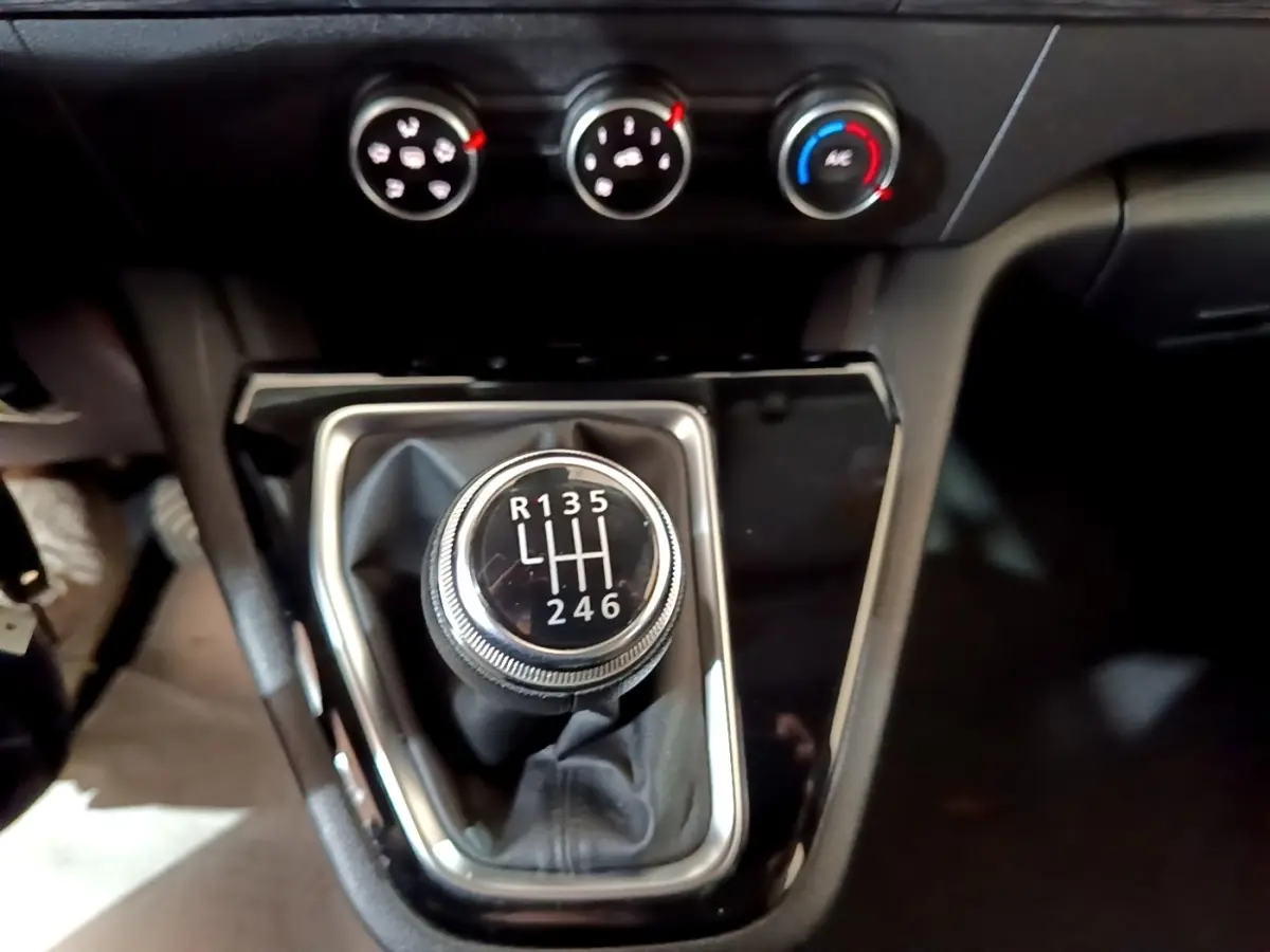 Gros plan sur le levier de vitesses manuel noir et chrome du Renault Kangoo blanc, avec commandes de climatisation en arrière-plan.