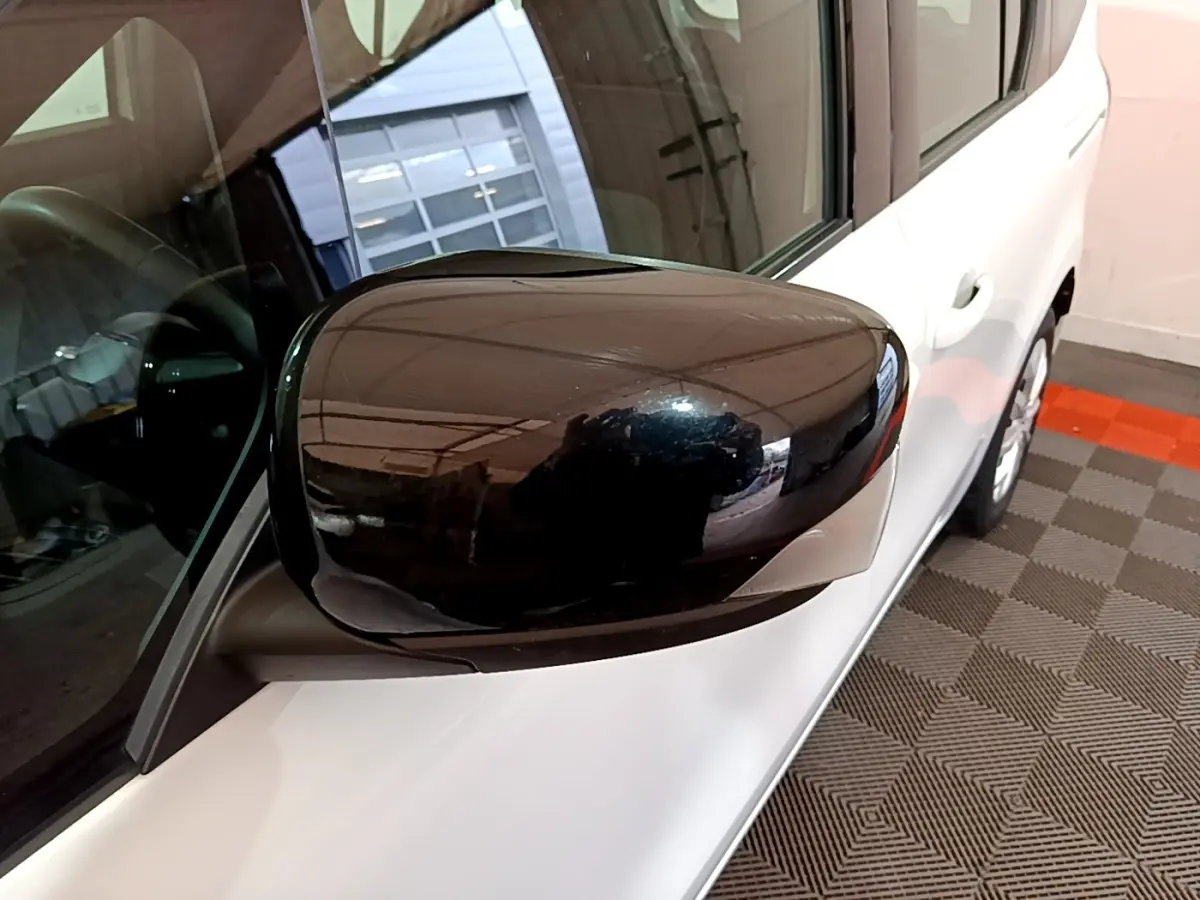 Gros plan sur le rétroviseur noir côté gauche d’un Renault Kangoo blanc, vue partielle du côté avant droit.