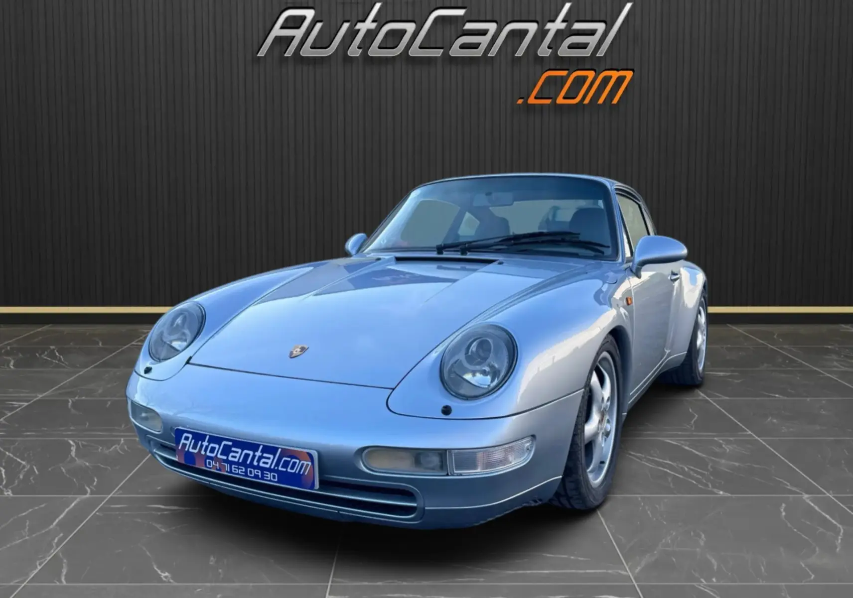 Porsche 911 Carrera 993 gris polaire vue 3/4 avant droite sur sol carrelé avec logo AutoCantal en arrière-plan.