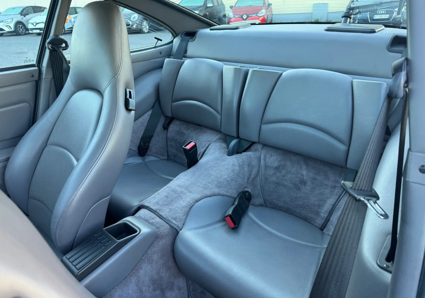 Vue intérieure arrière de la Porsche 911 Carrera 2 gris polaire de 1996, montrant les sièges en cuir gris et les ceintures de sécurité.
