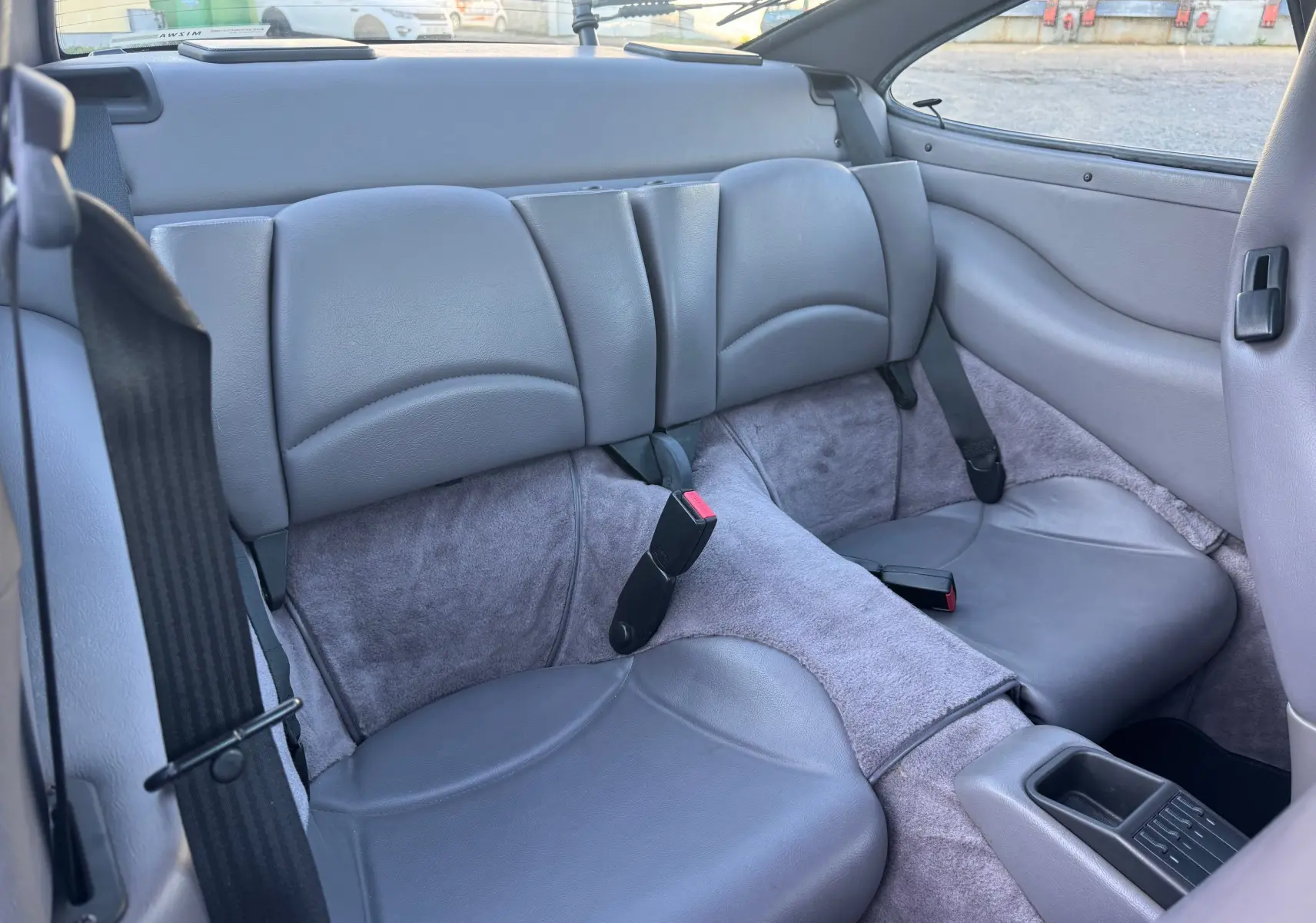 Vue intérieure arrière des sièges en cuir gris clair du Porsche 911 Carrera 993, soulignant l’espace et les ceintures de sécurité.