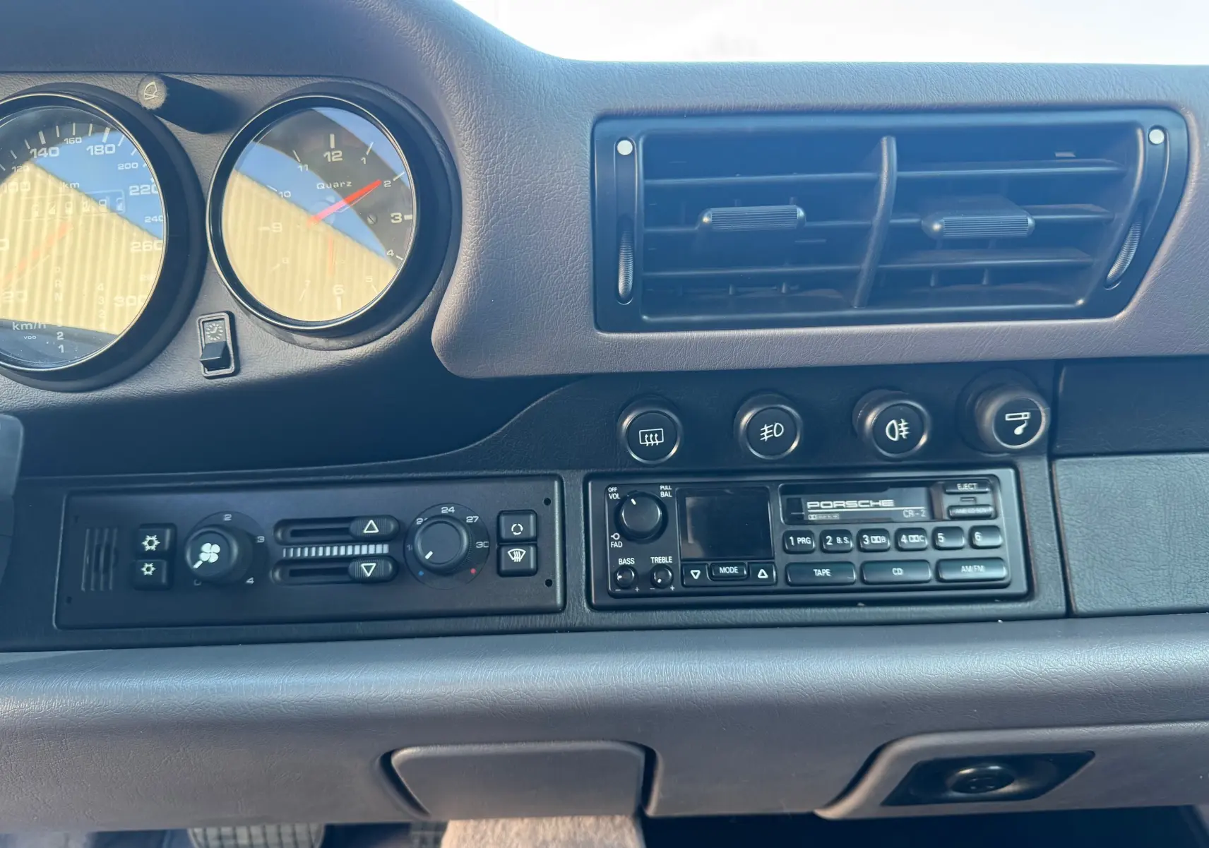 Vue rapprochée du tableau de bord gris d'une Porsche 911 Carrera 993 de 1996 avec commandes et radio d'origine.
