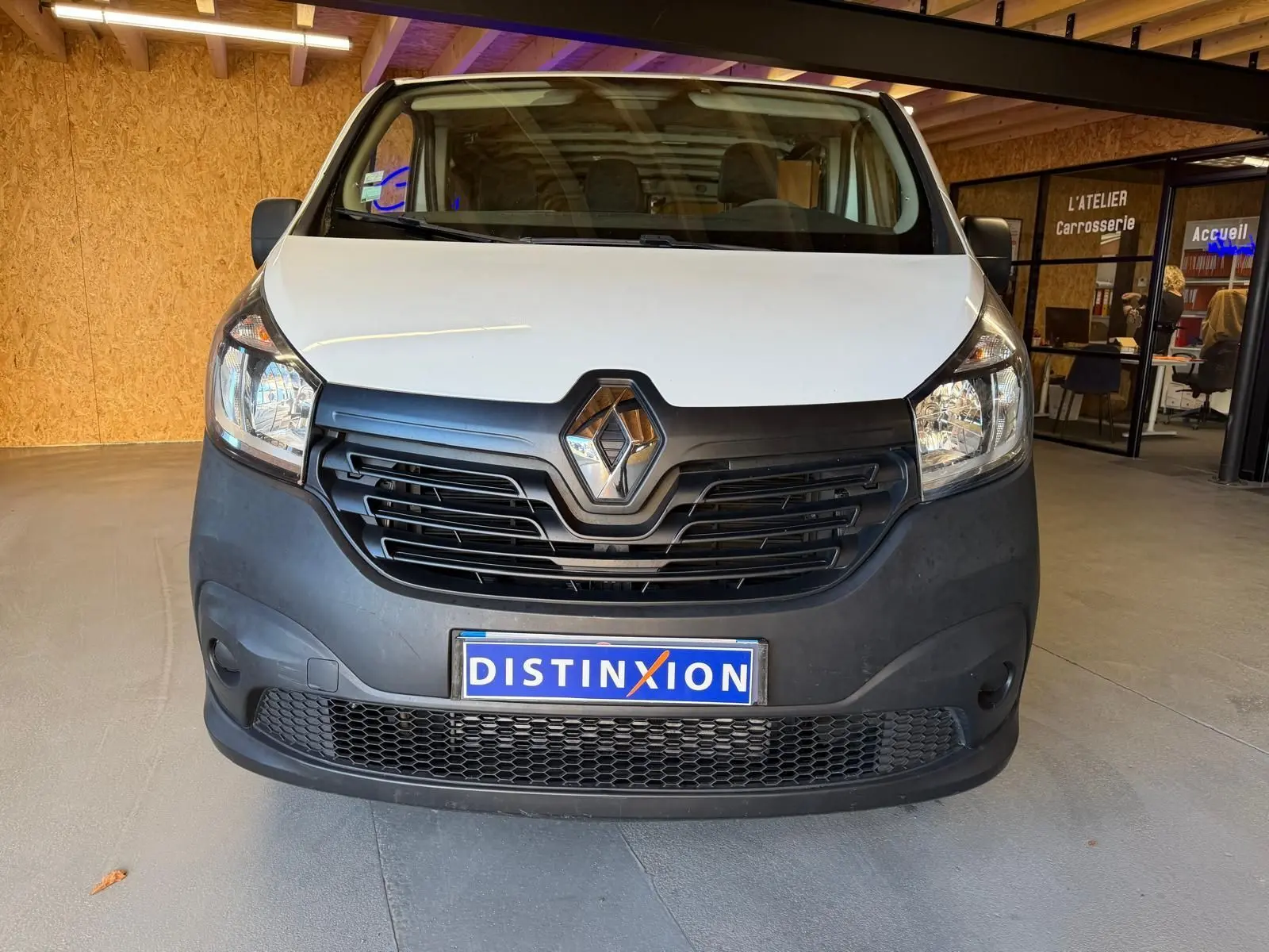 Vue de face d’un Renault Trafic Fourgon blanc de 2017 avec calandre noire et plaque Distinxion visible en intérieur.
