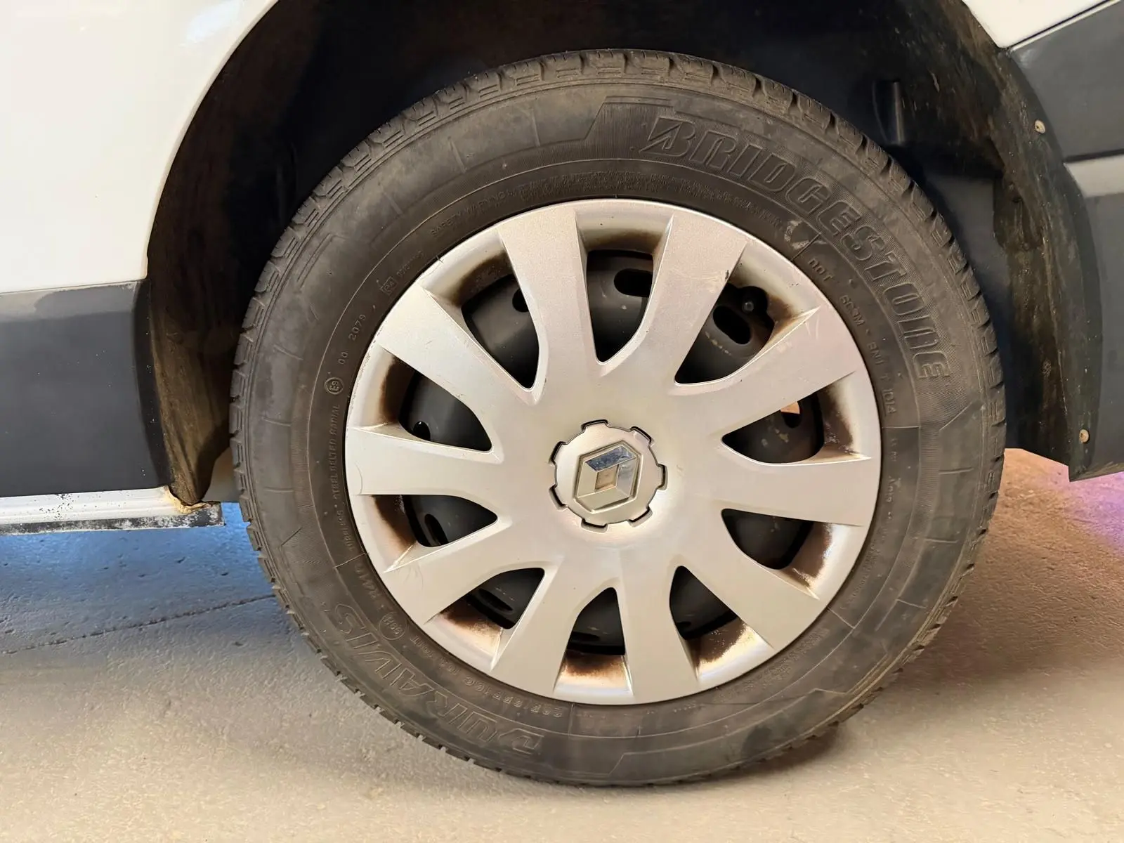 Gros plan sur la roue avant gauche blanche d’un Renault Trafic Fourgon 2017 avec jante en plastique gris clair.