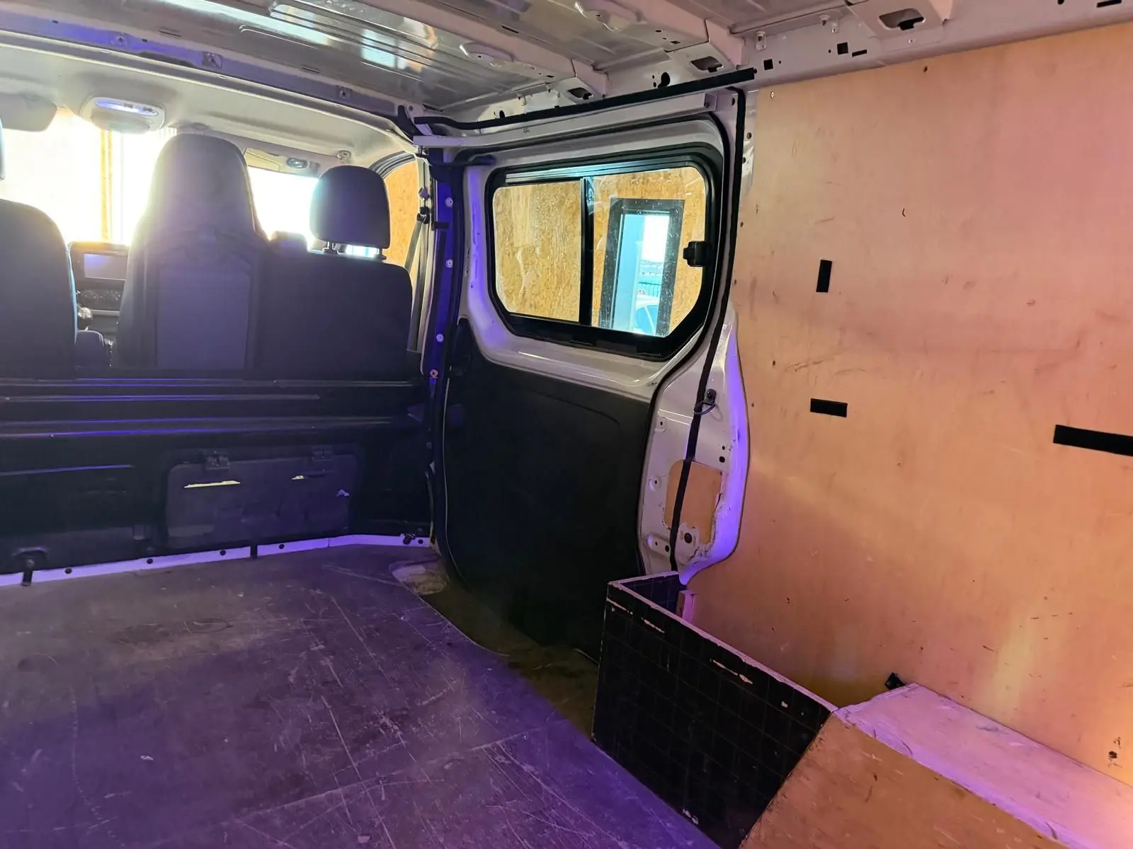 Vue intérieure arrière droite du Renault Trafic blanc avec habillage bois sur les parois et sièges avant visibles.