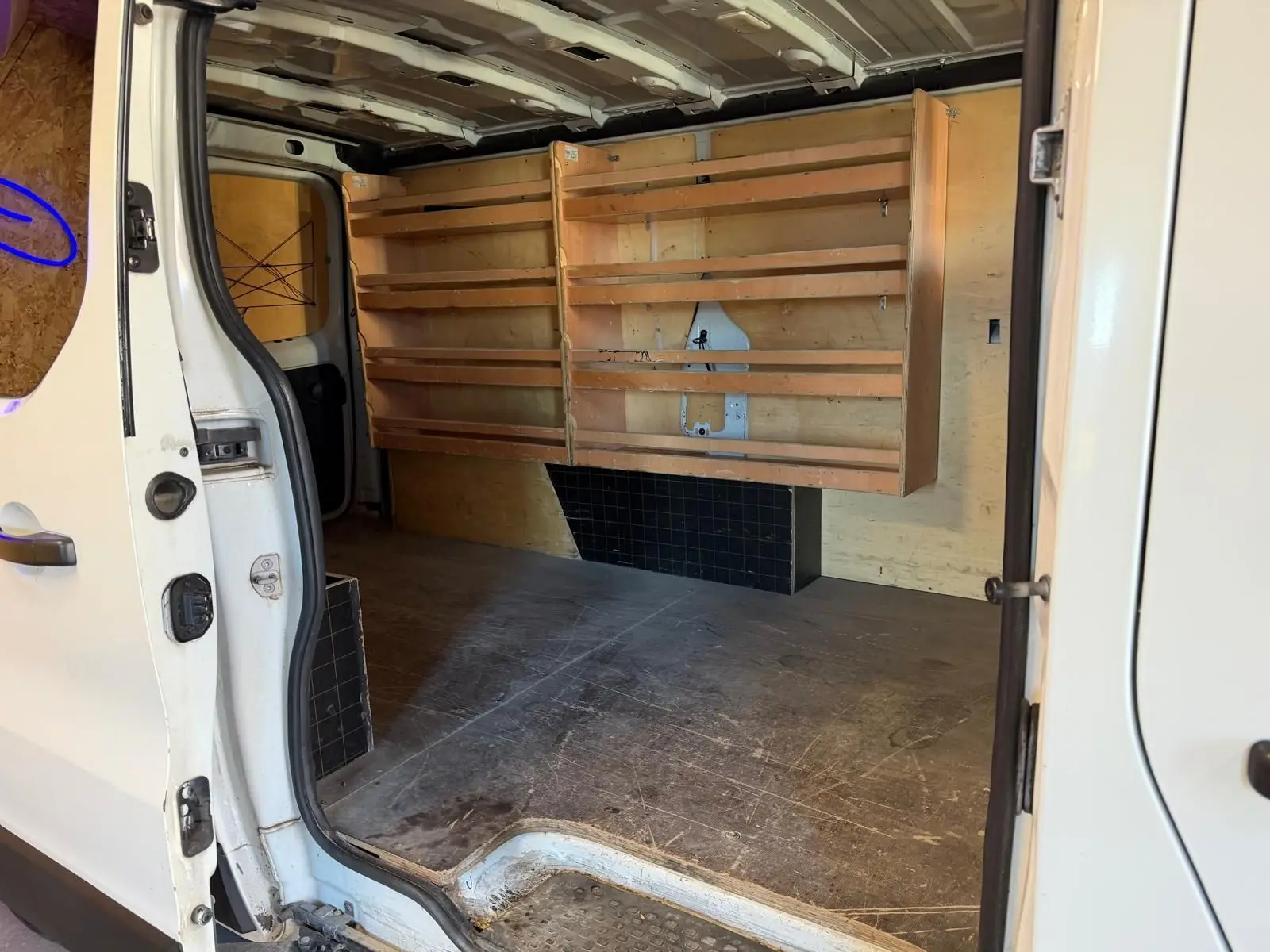 Vue intérieure côté droit du Renault Trafic blanc 2017 avec habillage bois et étagères dans l’espace de chargement.