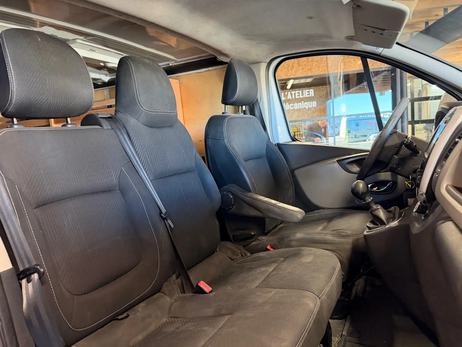 Vue intérieure côté conducteur du Renault Trafic Fourgon blanc, montrant les sièges noirs et le levier de vitesses manuel.