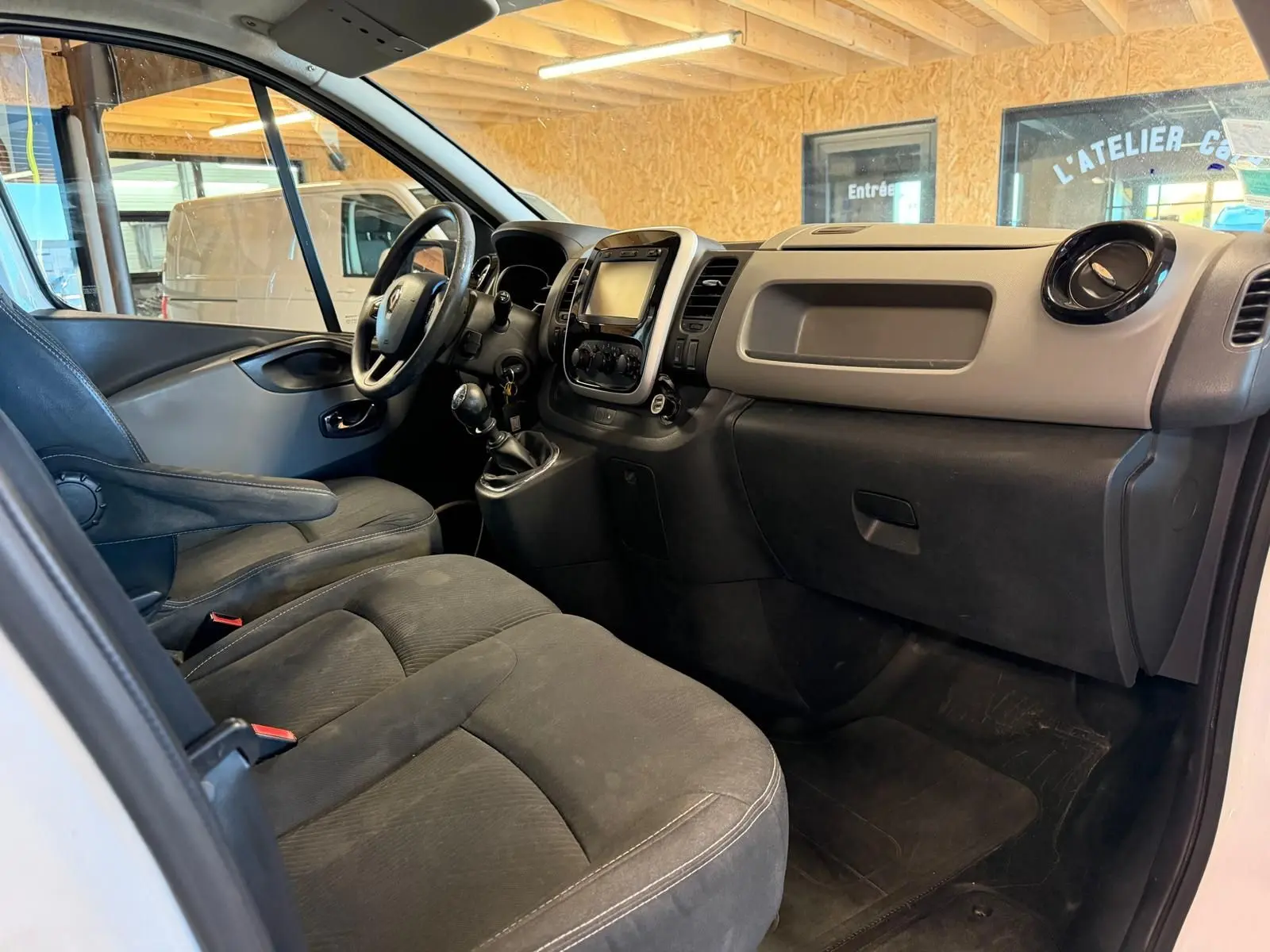 Vue intérieure côté conducteur du Renault Trafic Fourgon blanc, mettant en valeur le tableau de bord et les sièges en tissu noir.