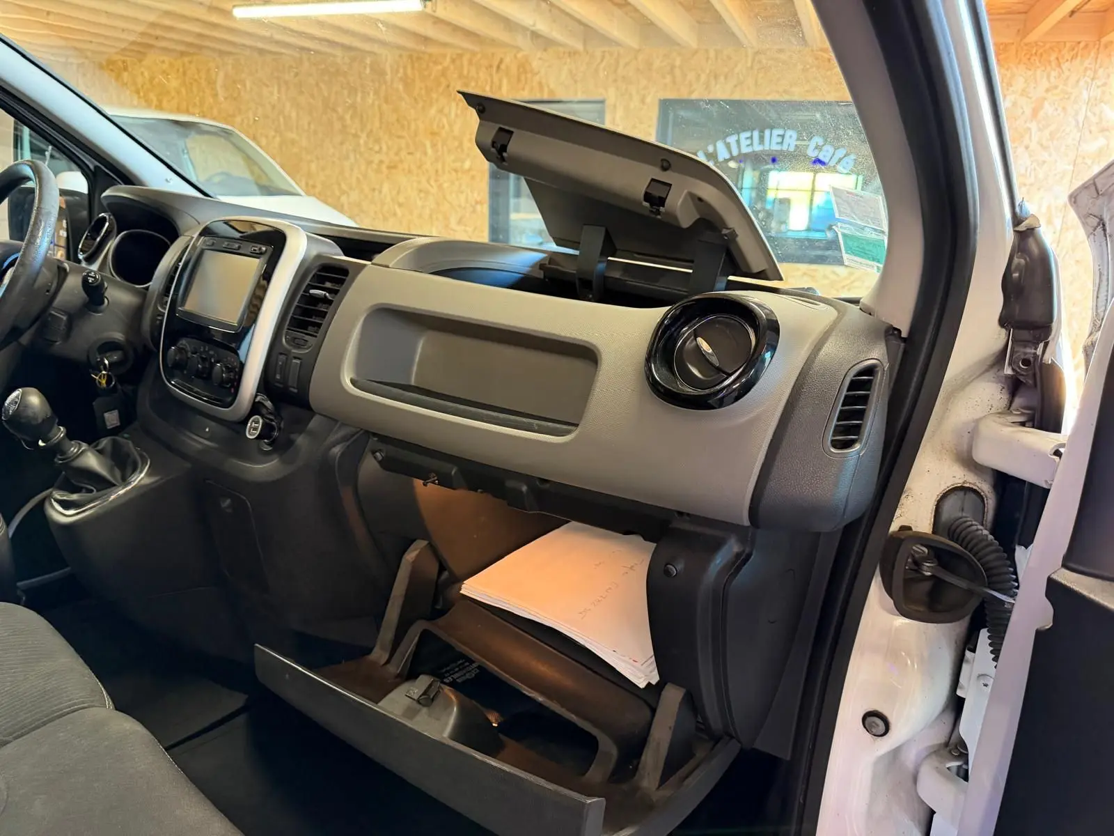 Vue intérieure côté passager du Renault Trafic Fourgon blanc 2017, tableau de bord avec boîte à gants ouverte et habillage bois visible.
