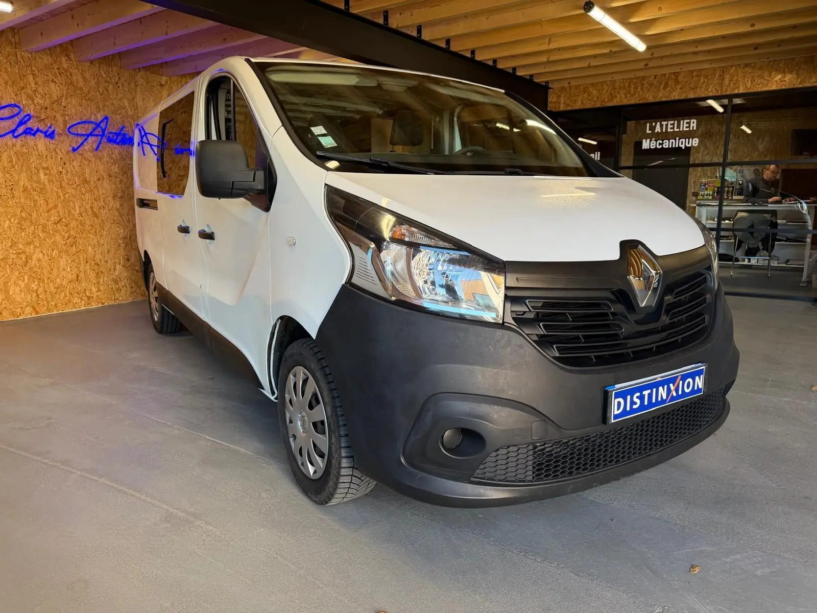 Renault Trafic Fourgon blanc en 3/4 avant droit, avec pare-chocs noir et intérieur habillage bois visible.