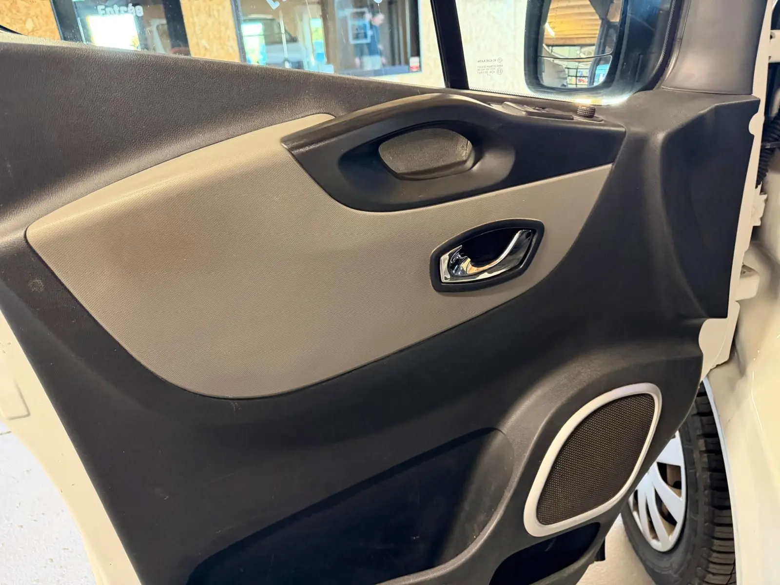 Vue intérieure côté gauche de la porte avant d’un Renault Trafic blanc, avec habillage bois et haut-parleur intégré.