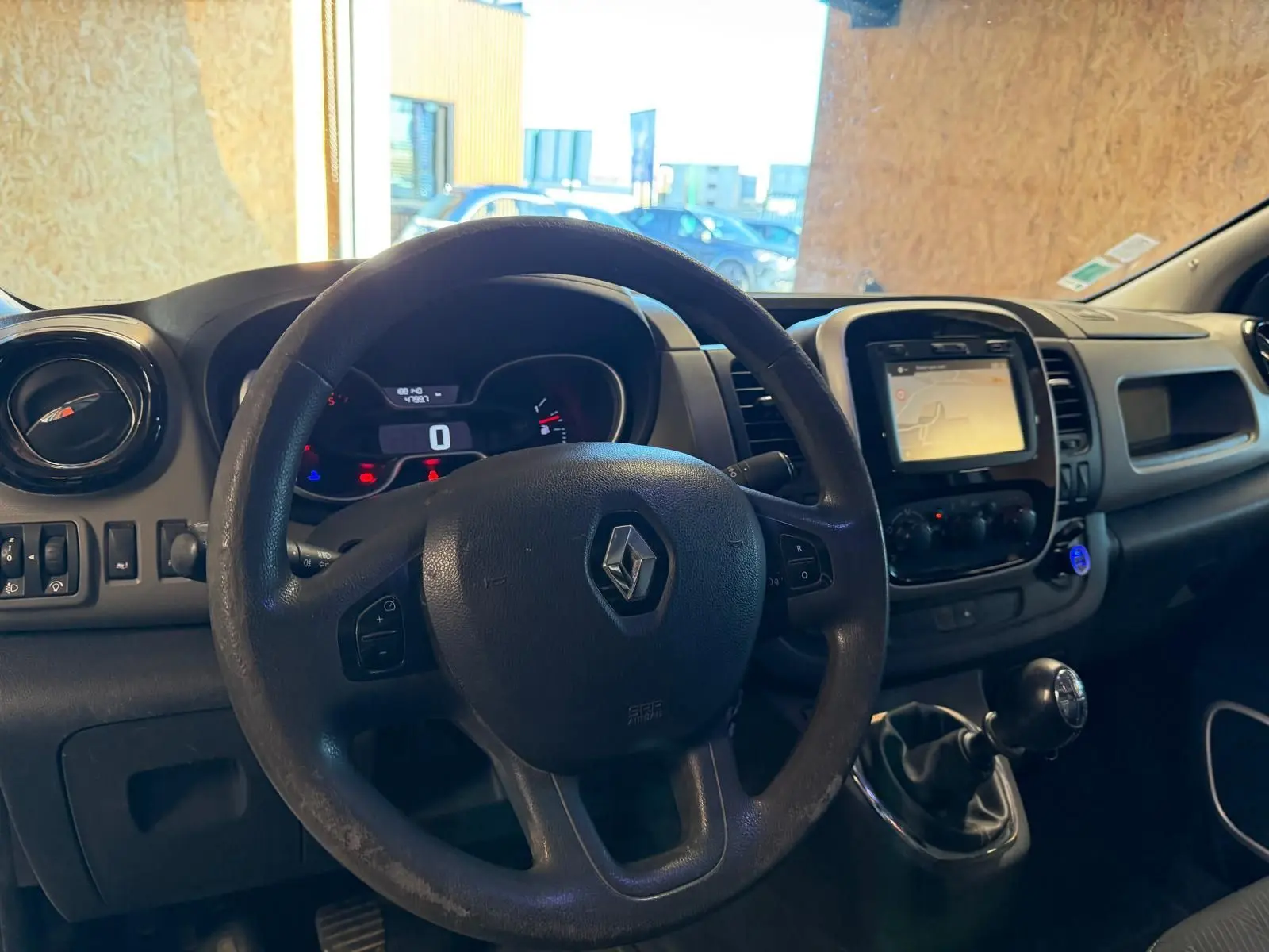 Vue intérieure du tableau de bord du Renault Trafic Fourgon blanc 2017, avec volant, écran GPS et levier de vitesses manuel.