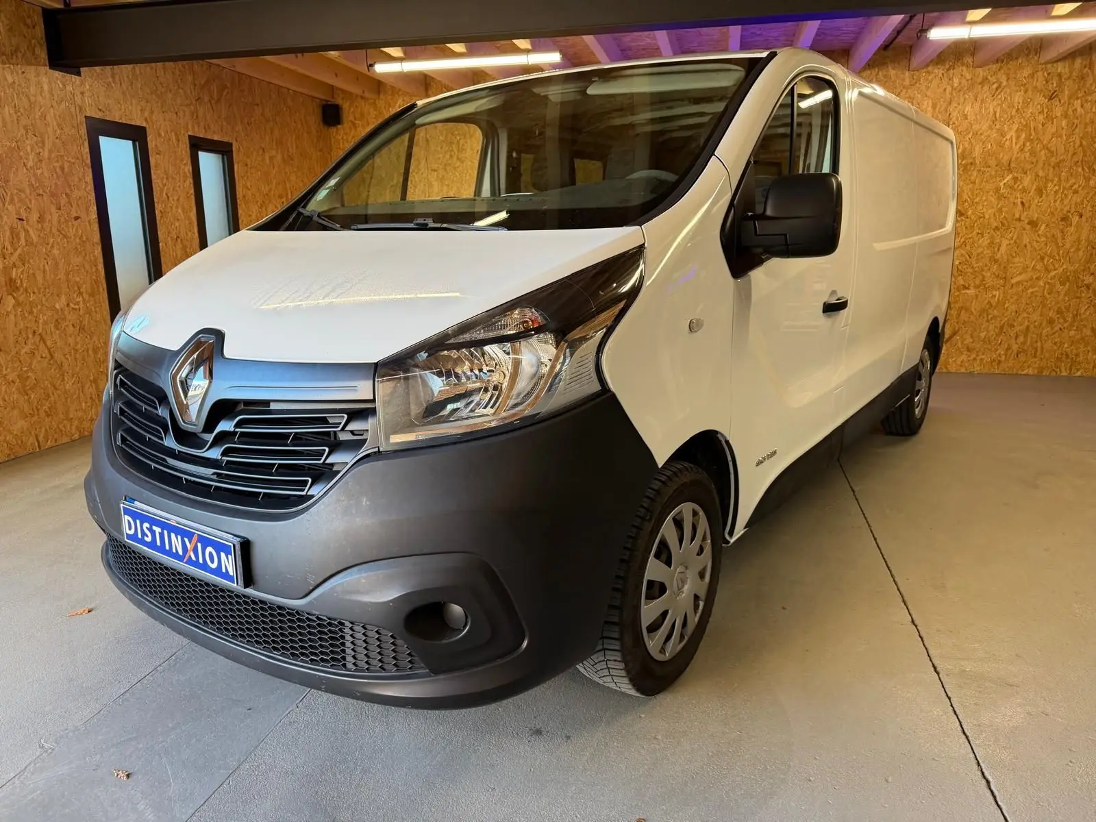 Renault Trafic Fourgon blanc en 3/4 avant droit, avec pare-chocs noir et intérieur habillage bois visible.