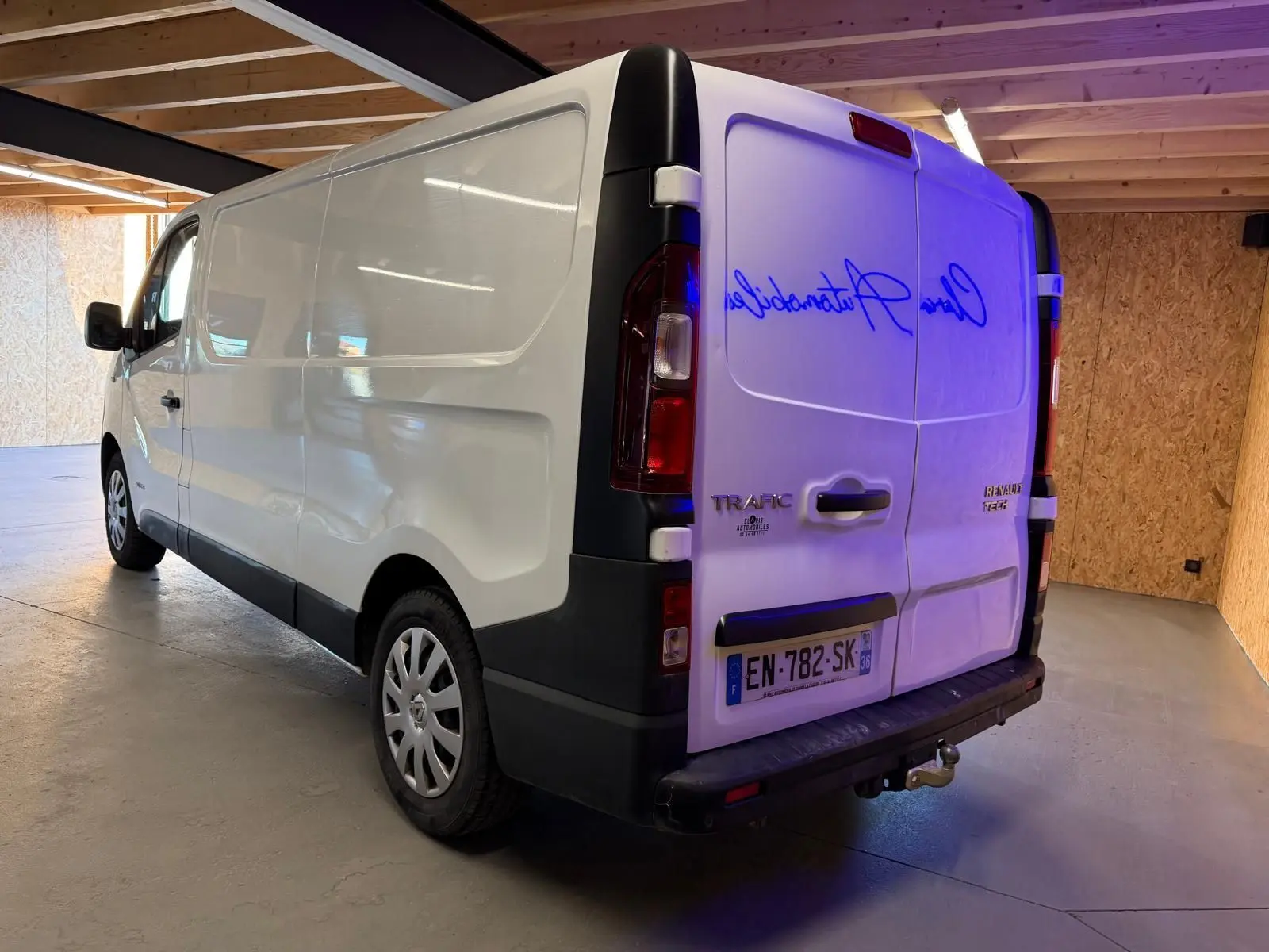 Vue 3/4 arrière droite du Renault Trafic Fourgon blanc de 2017 avec attelage et habillage bois visible en intérieur.