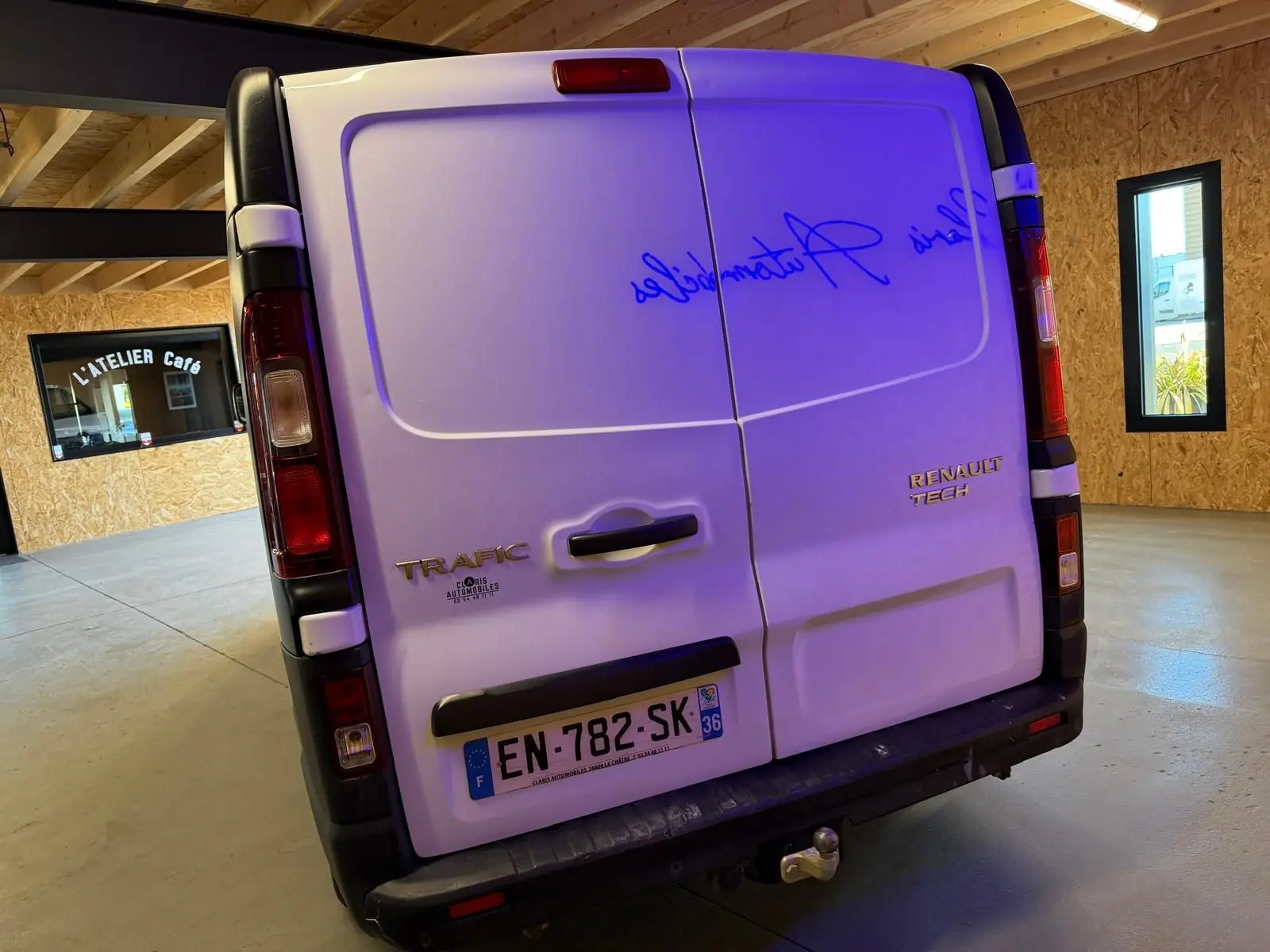 Vue arrière d'un Renault Trafic fourgon blanc de 2017 avec attelage, dans un garage au sol béton.