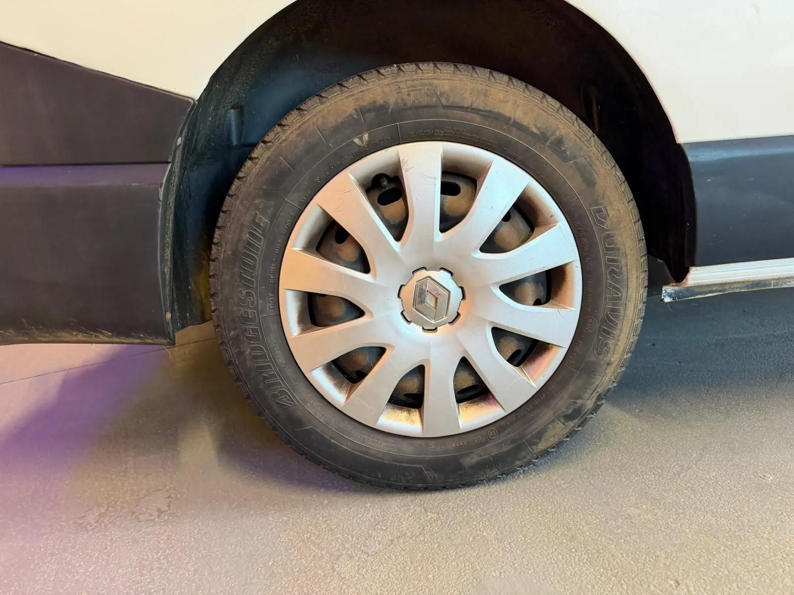 Gros plan sur la roue avant gauche d’un Renault Trafic blanc, avec jante en alliage et logo Renault visible.