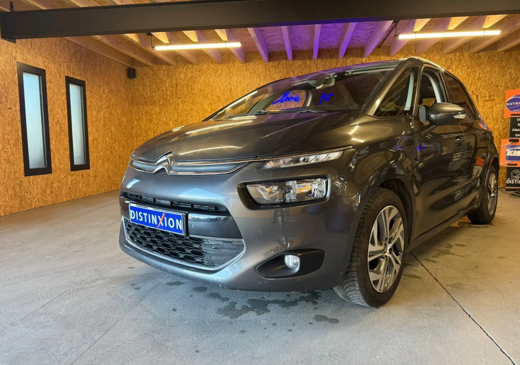 Vue 3/4 avant droit d'une Citroën C4 Picasso gris métallisé dans un showroom avec éclairage intérieur.
