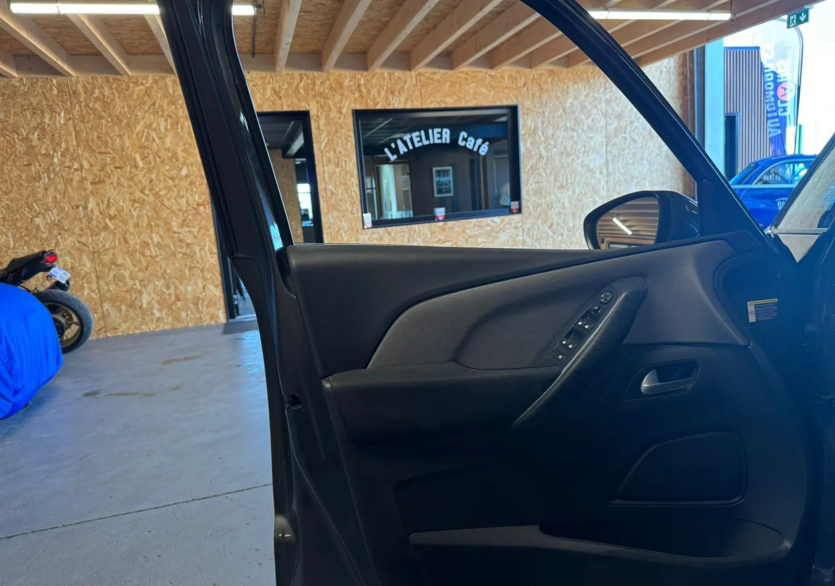 Vue intérieure côté gauche de la porte avant ouverte d'une Citroën C4 Picasso gris, avec commandes de vitres et rétroviseur.