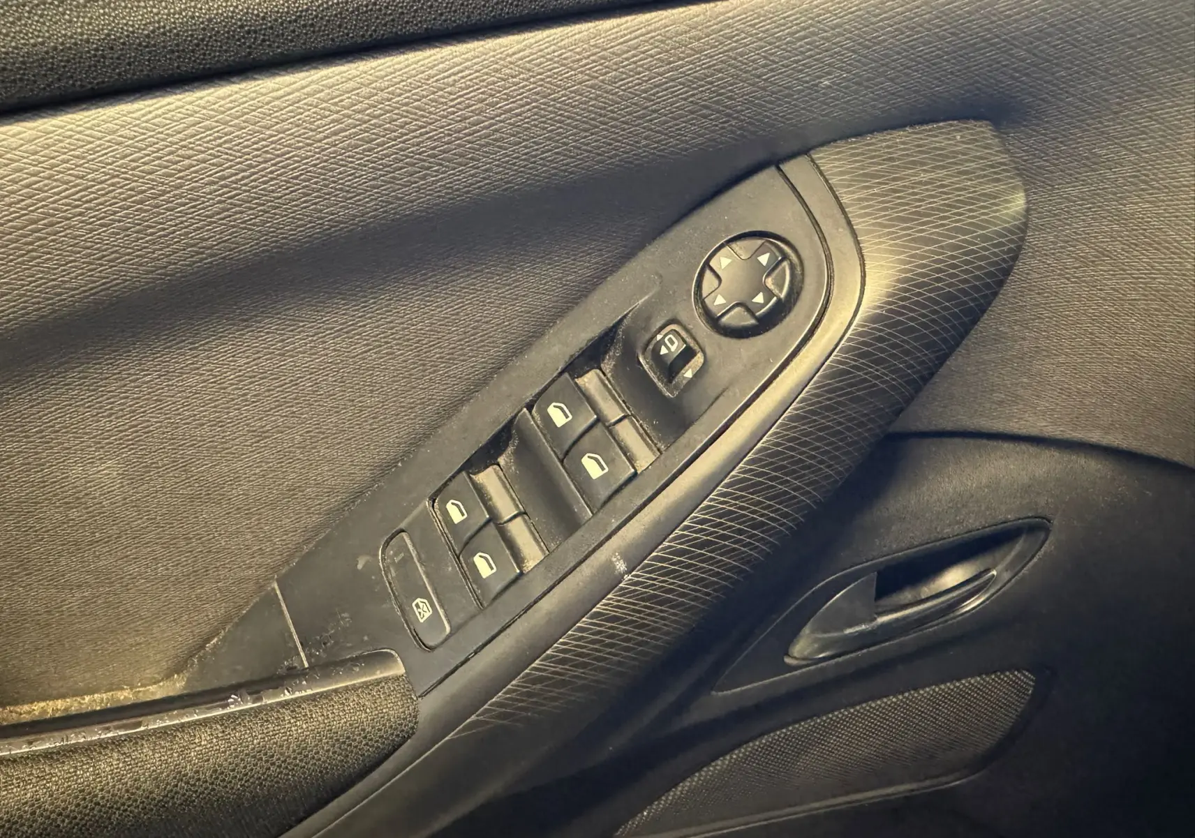 Gros plan sur la commande des vitres et rétroviseurs côté conducteur de la porte intérieure noire du Citroën C4 Picasso 2016.