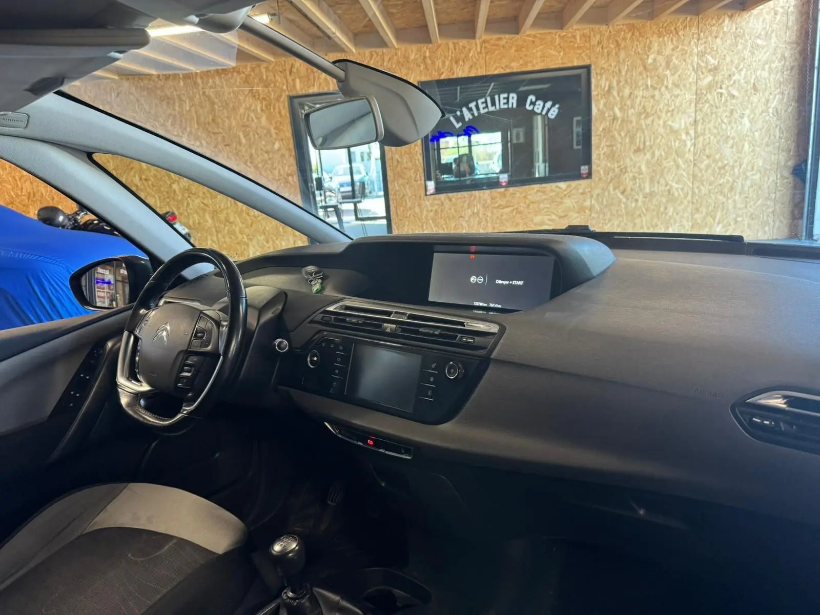 Vue intérieure côté conducteur du Citroën C4 Picasso gris, volant cuir multifonctions et écran central allumé.