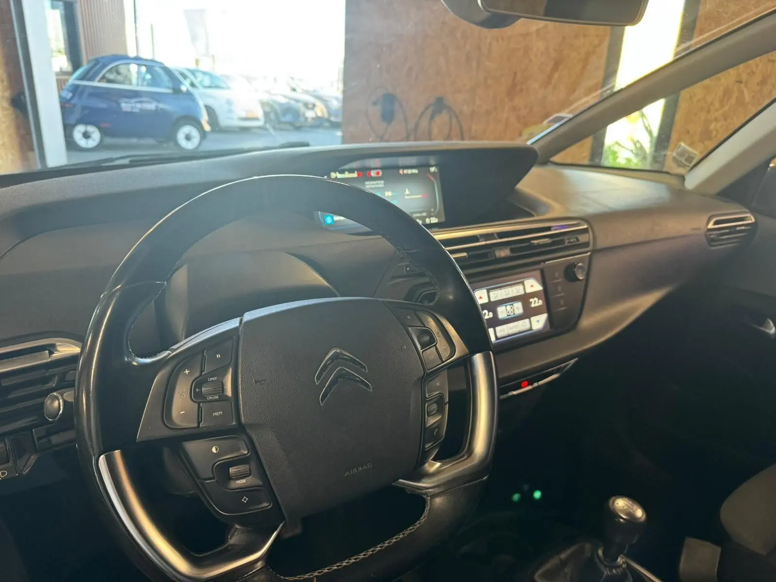 Vue intérieure centrée sur le volant cuir multifonctions et tableau de bord numérique de la Citroën C4 Picasso gris.