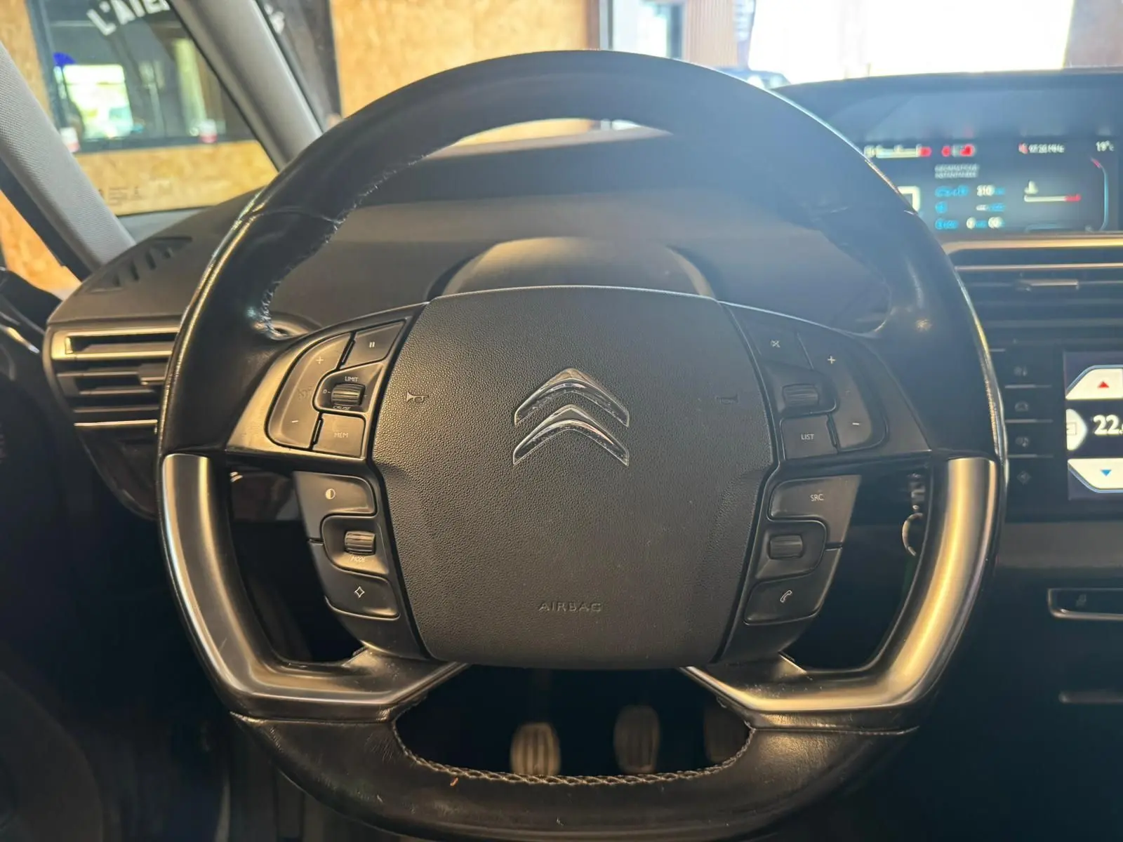 Vue rapprochée du volant cuir multifonctions noir de la Citroën C4 Picasso 2016 avec tableau de bord numérique en arrière-plan.