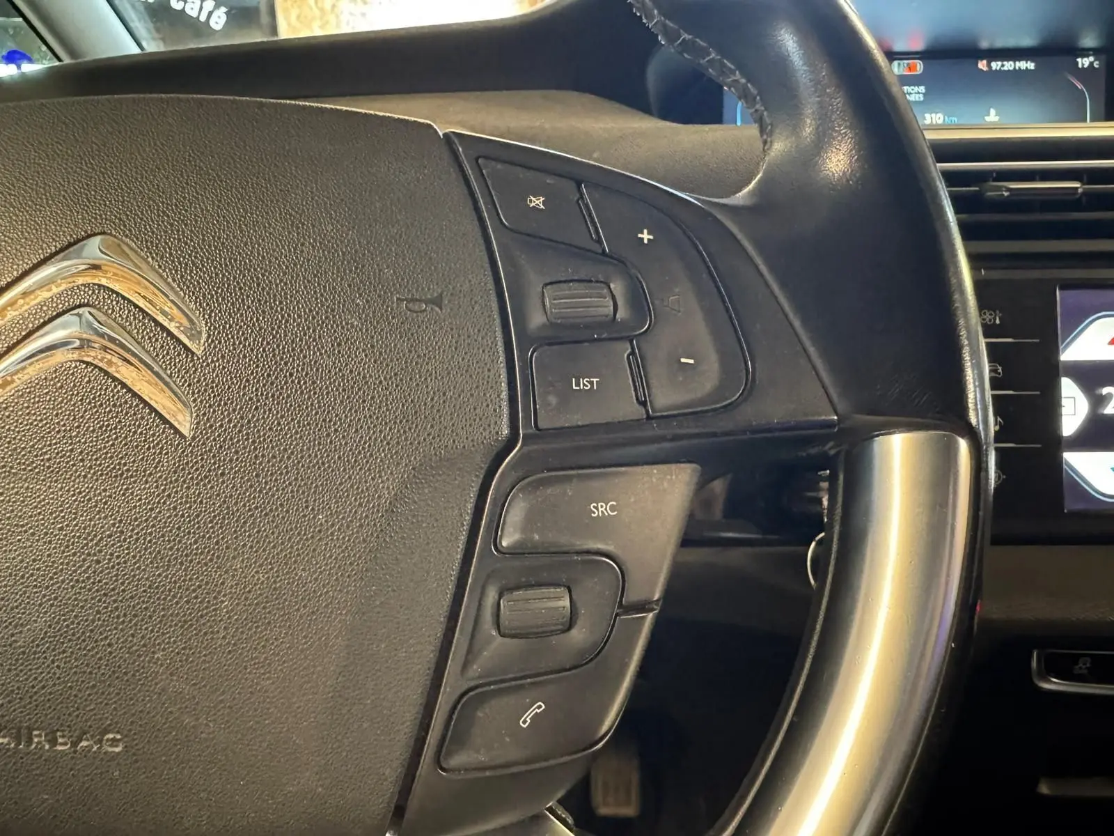 Gros plan sur le volant cuir multifonctions noir d'une Citroën C4 Picasso 2016 avec commandes audio et écran de bord en arrière-plan.