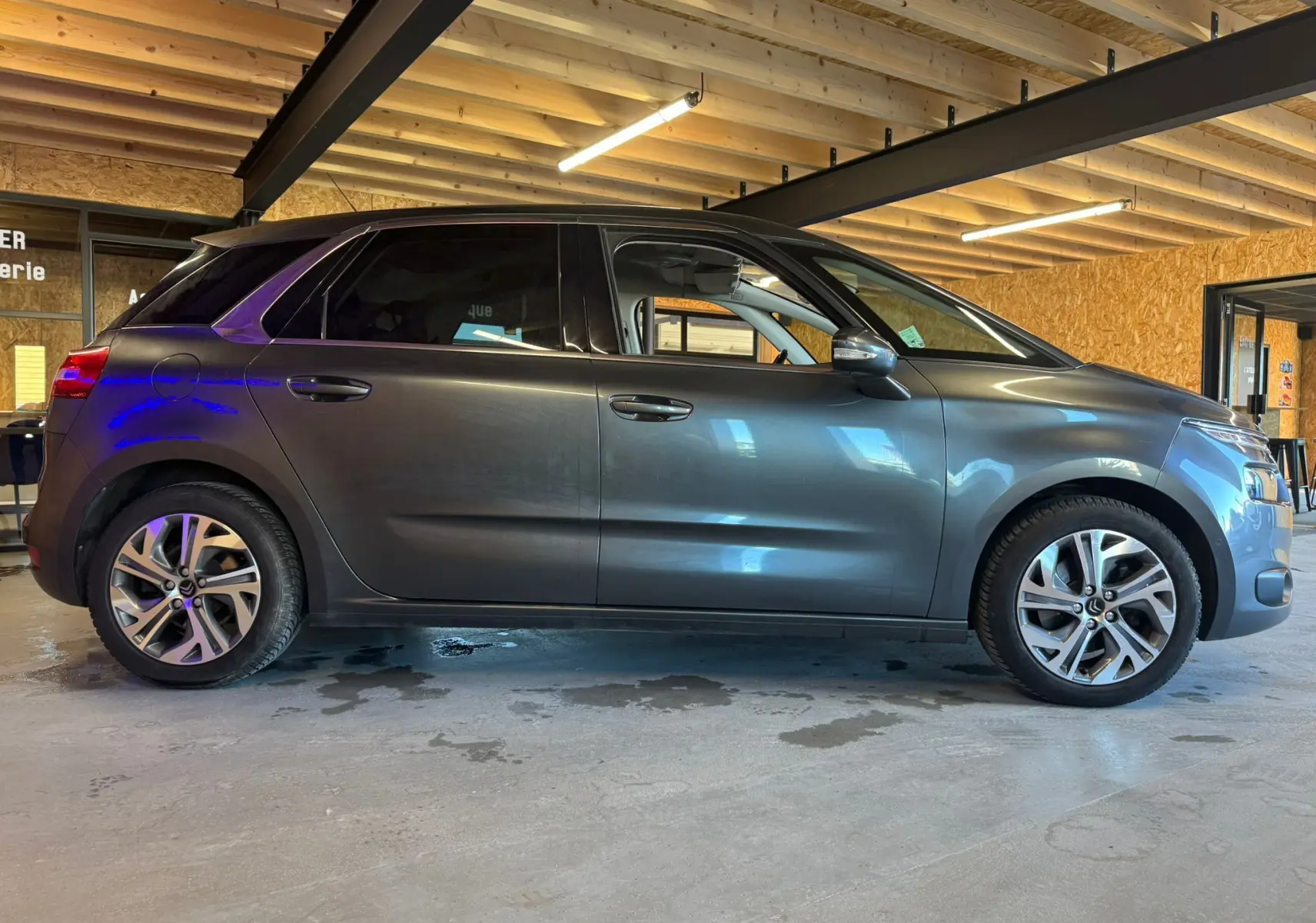 Vue de profil côté gauche d'une Citroën C4 Picasso gris métallisé avec jantes alu dans un garage éclairé.