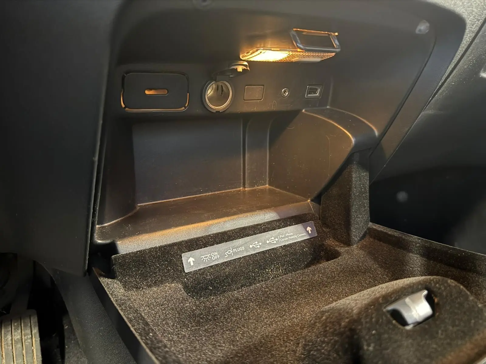 Vue rapprochée de la boîte à gants noire du Citroën C4 Picasso 2016 avec prise allume-cigare et éclairage intérieur.