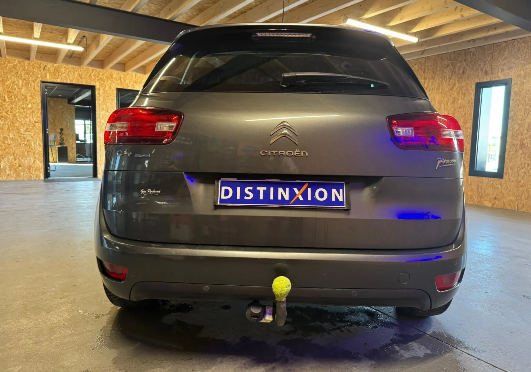 Vue arrière d'une Citroën C4 Picasso gris métallisé avec attelage et feux rouges dans un garage lumineux.
