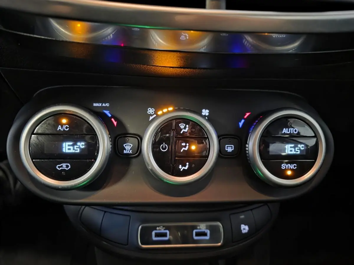 Gros plan sur la commande de climatisation bi-zone avec affichage digital à 16,5°C et ports USB du Fiat 500X rouge 2024.