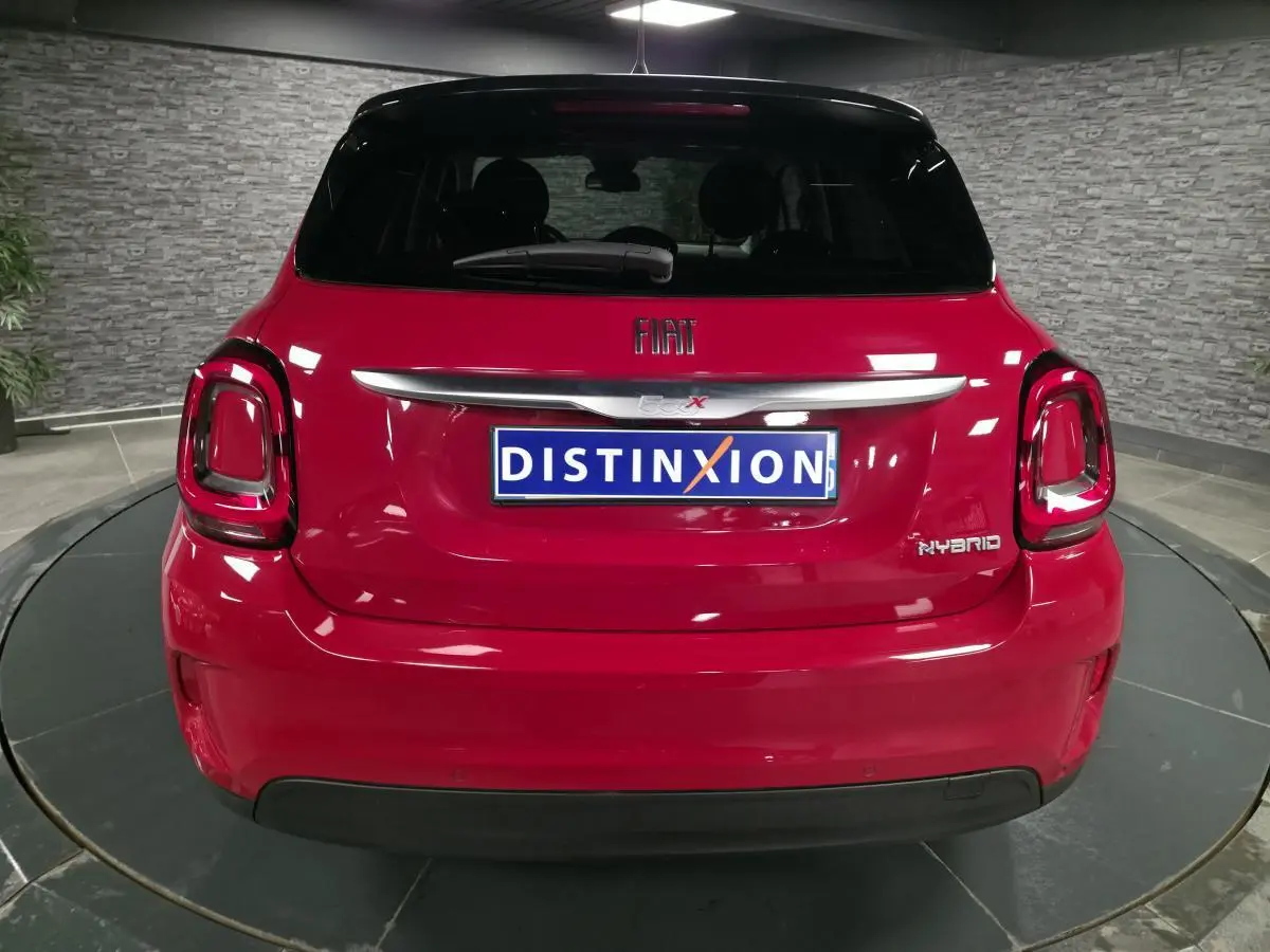 Vue arrière d'une Fiat 500X rouge Passion avec toit noir et badges Hybrid, dans un showroom intérieur.