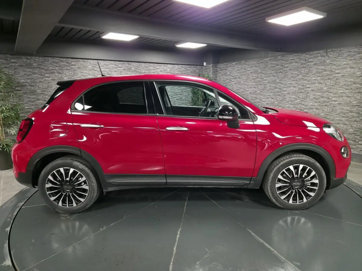 Profil droit d'une Fiat 500X rouge Passion avec jantes alliage 17'' et rétroviseurs noirs dans un showroom.