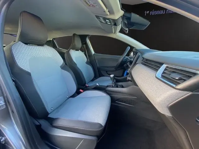 Vue intérieure côté conducteur de la Renault Clio gris foncé 2025, sièges tissu bicolore et tableau de bord moderne.