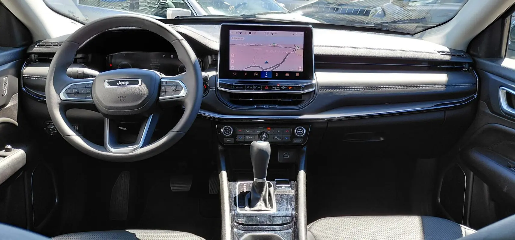 Vue frontale de l’intérieur noir du Jeep Compass 2025 avec volant multifonction et écran tactile central.
