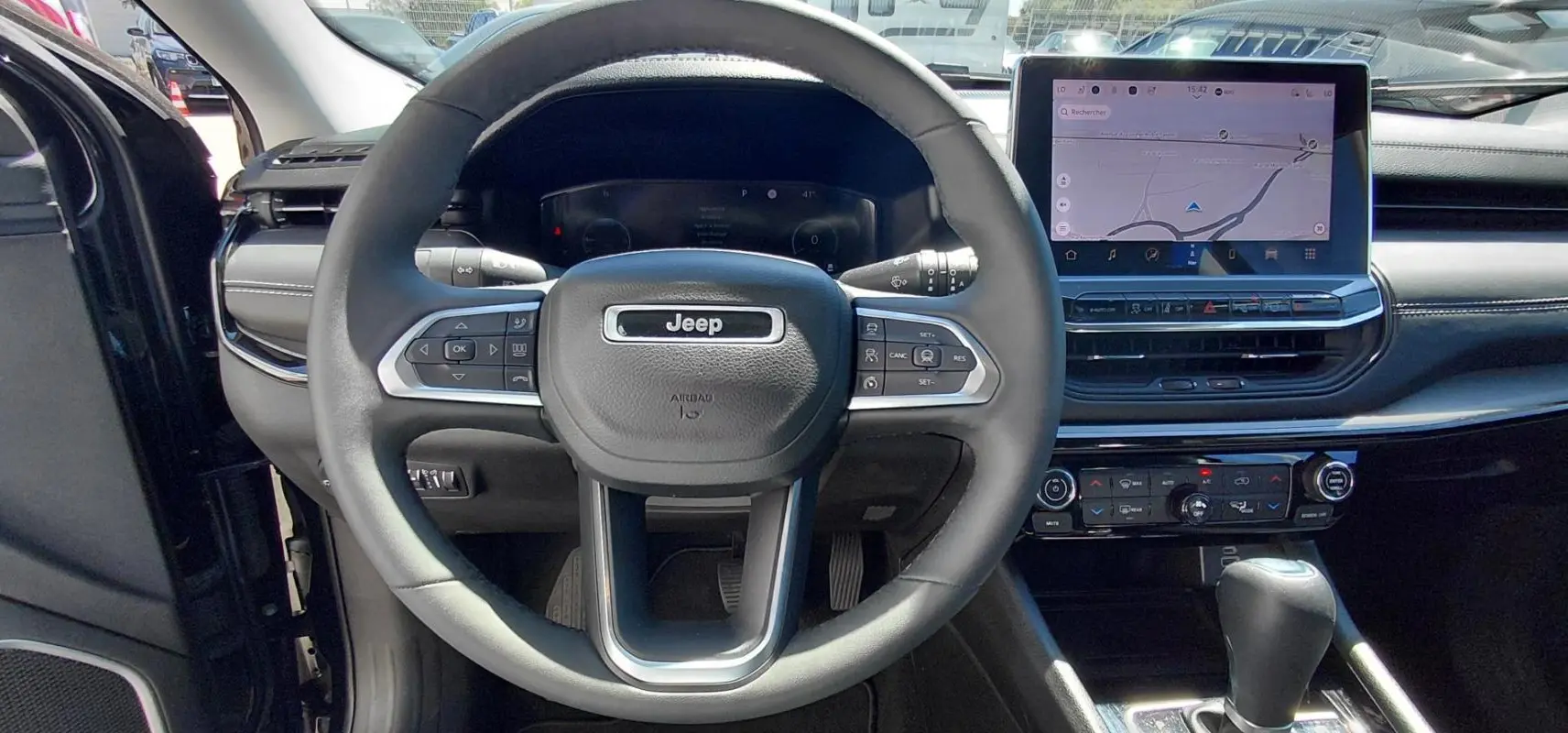 Vue intérieure centrée sur le volant Jeep noir et l'écran tactile du tableau de bord du Compass 2025.