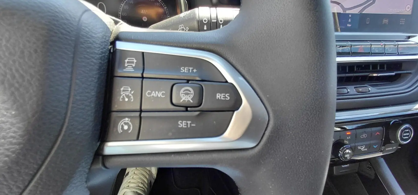 Gros plan sur les commandes du volant noir du Jeep Compass 2025, avec tableau de bord et console centrale en arrière-plan.