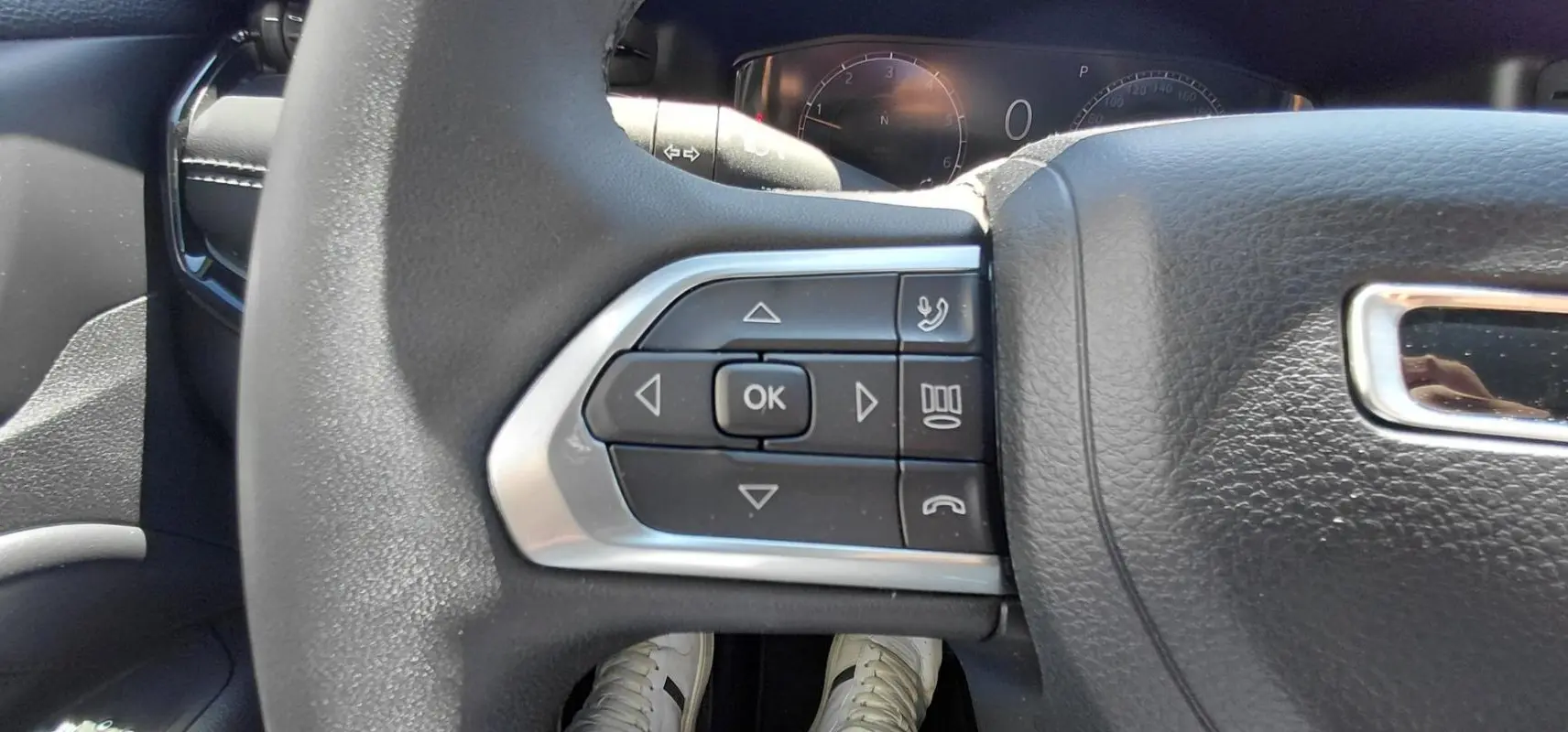 Gros plan sur les commandes multifonctions à gauche du volant noir du Jeep Compass 2025, avec tableau de bord en arrière-plan.