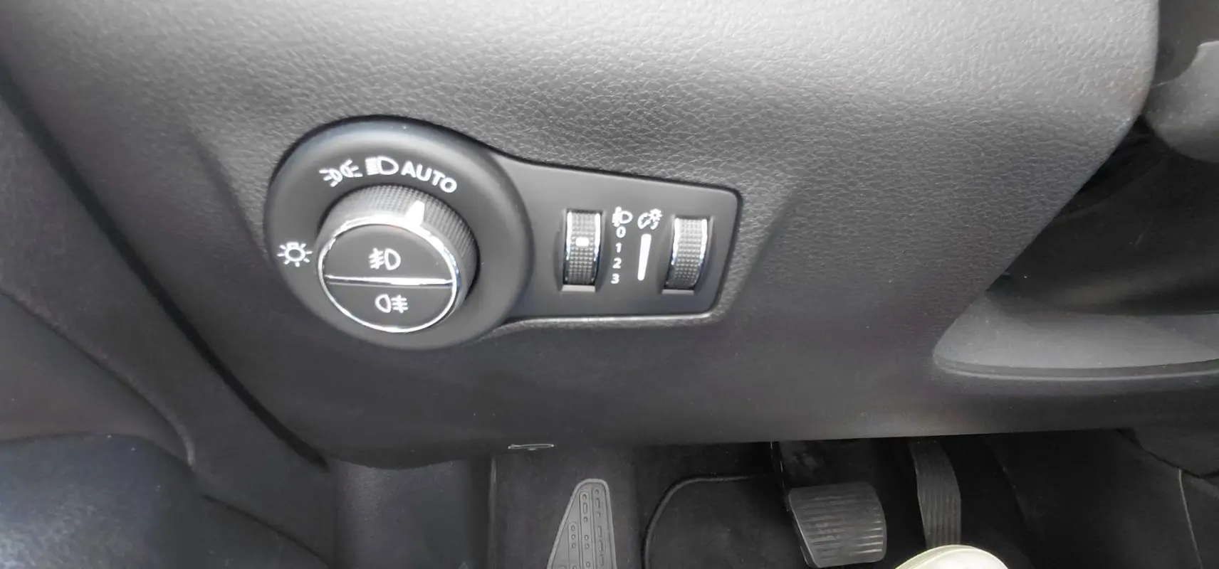 Gros plan sur les commandes d’éclairage et réglages du tableau de bord du Jeep Compass noir, côté conducteur.