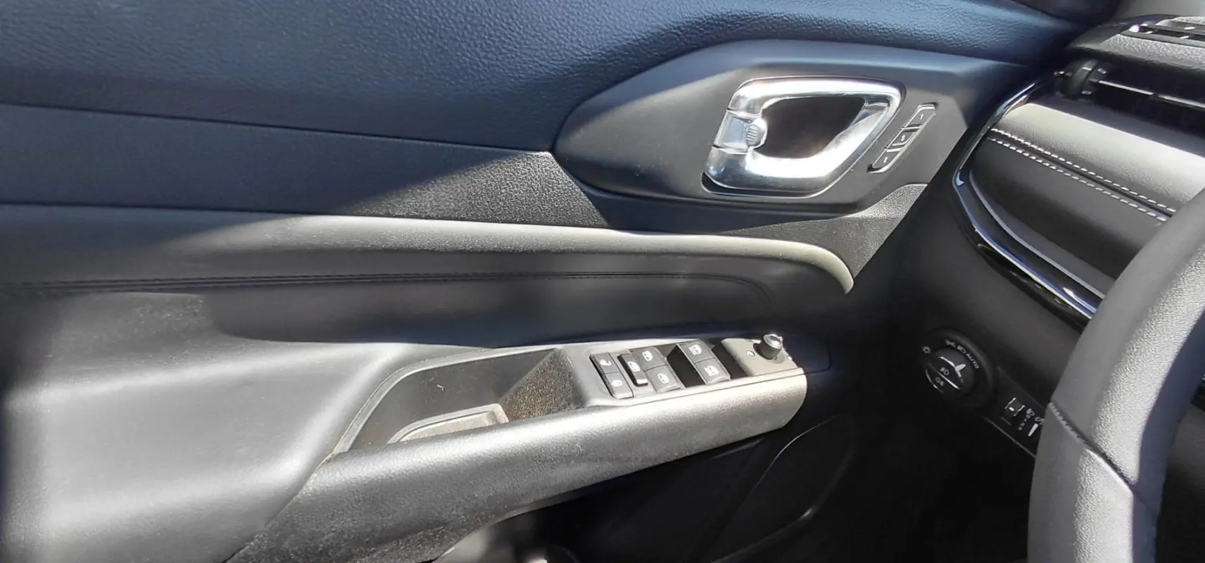 Détail de la porte côté conducteur du Jeep Compass 2025 noir, avec commandes des vitres et poignée chromée.