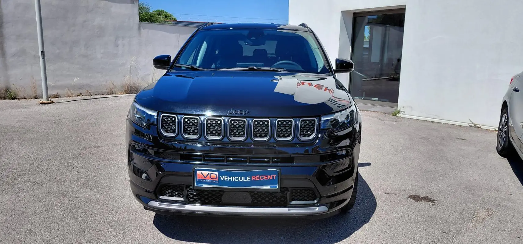 Vue frontale d'un Jeep Compass noir 2025 avec calandre distinctive et phares LED allumés, stationné en extérieur.