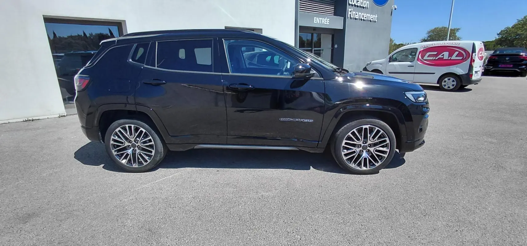 Jeep Compass noir vu de profil côté gauche, avec jantes alliage 19 pouces et barres de toit visibles.