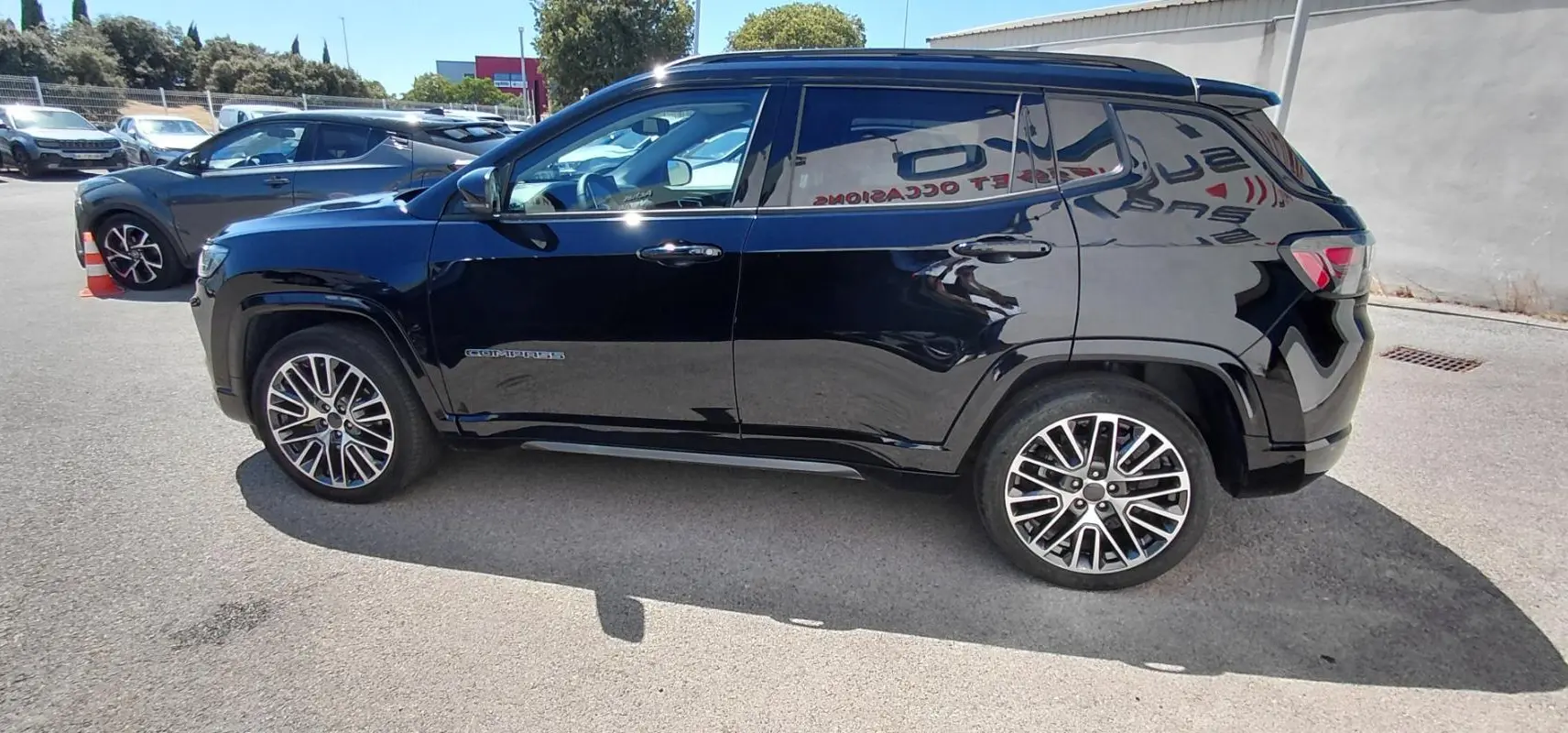 Jeep Compass noir vu de profil côté gauche, avec jantes alliage 19 pouces et barres de toit visibles.