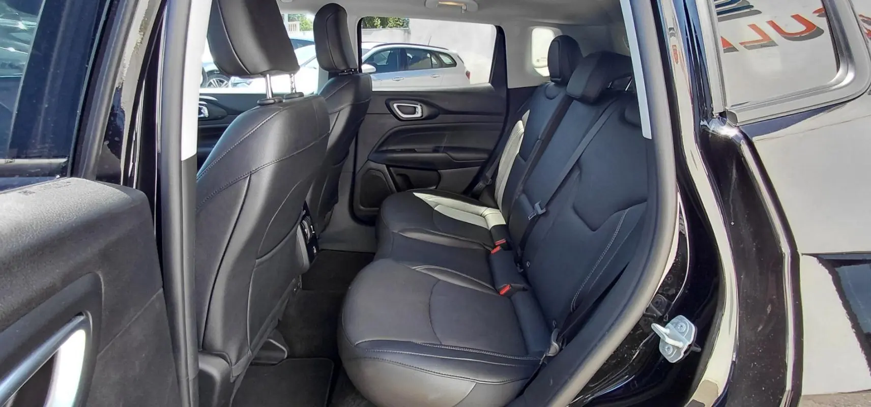 Vue intérieure côté gauche des sièges arrière en cuir noir du Jeep Compass 2025 noir avec accoudoir central et finitions contrastées.
