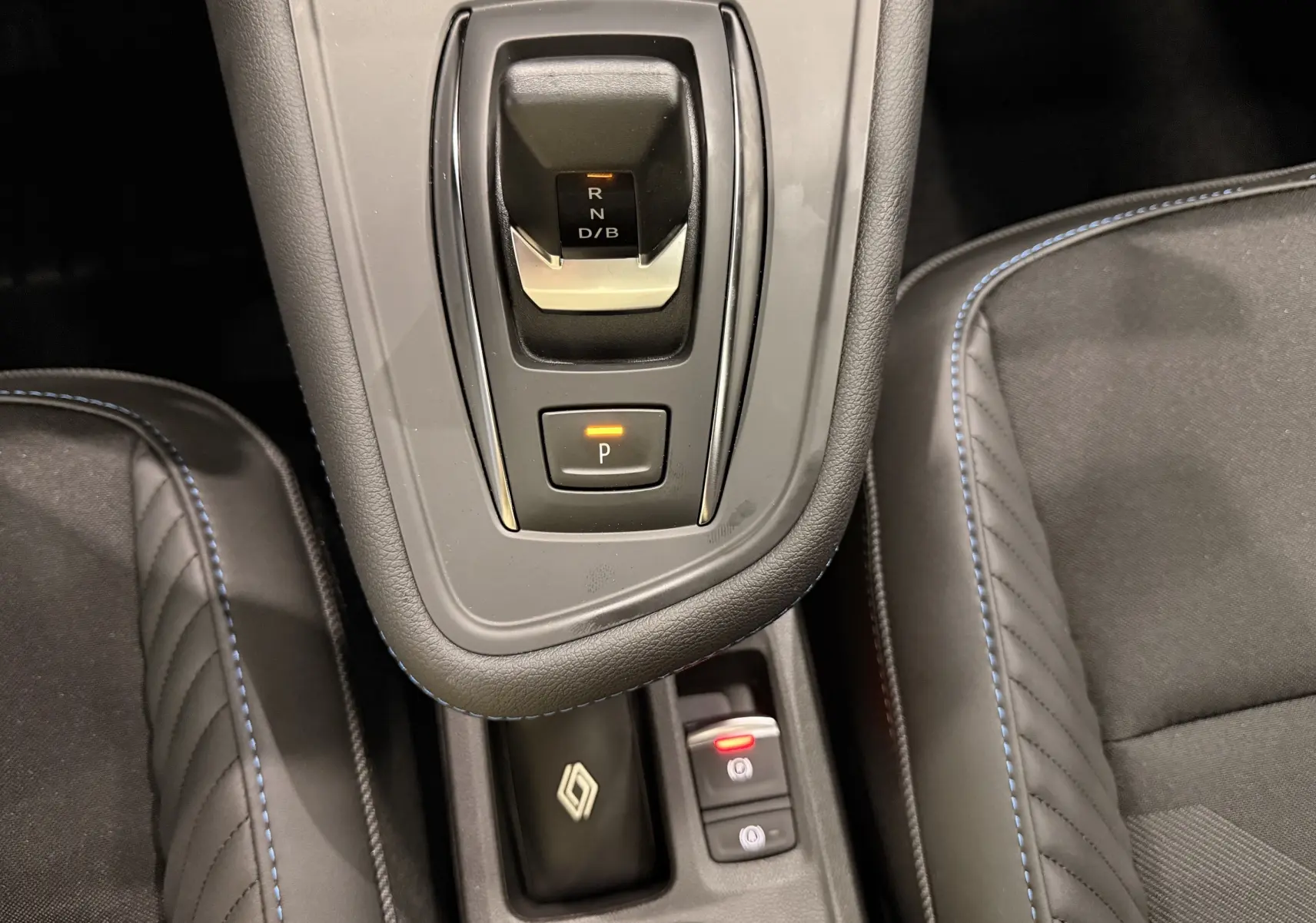 Vue rapprochée de la console centrale du Renault SYMBIOZ gris, avec levier de vitesses automatique et sièges noirs à surpiqûres bleues.