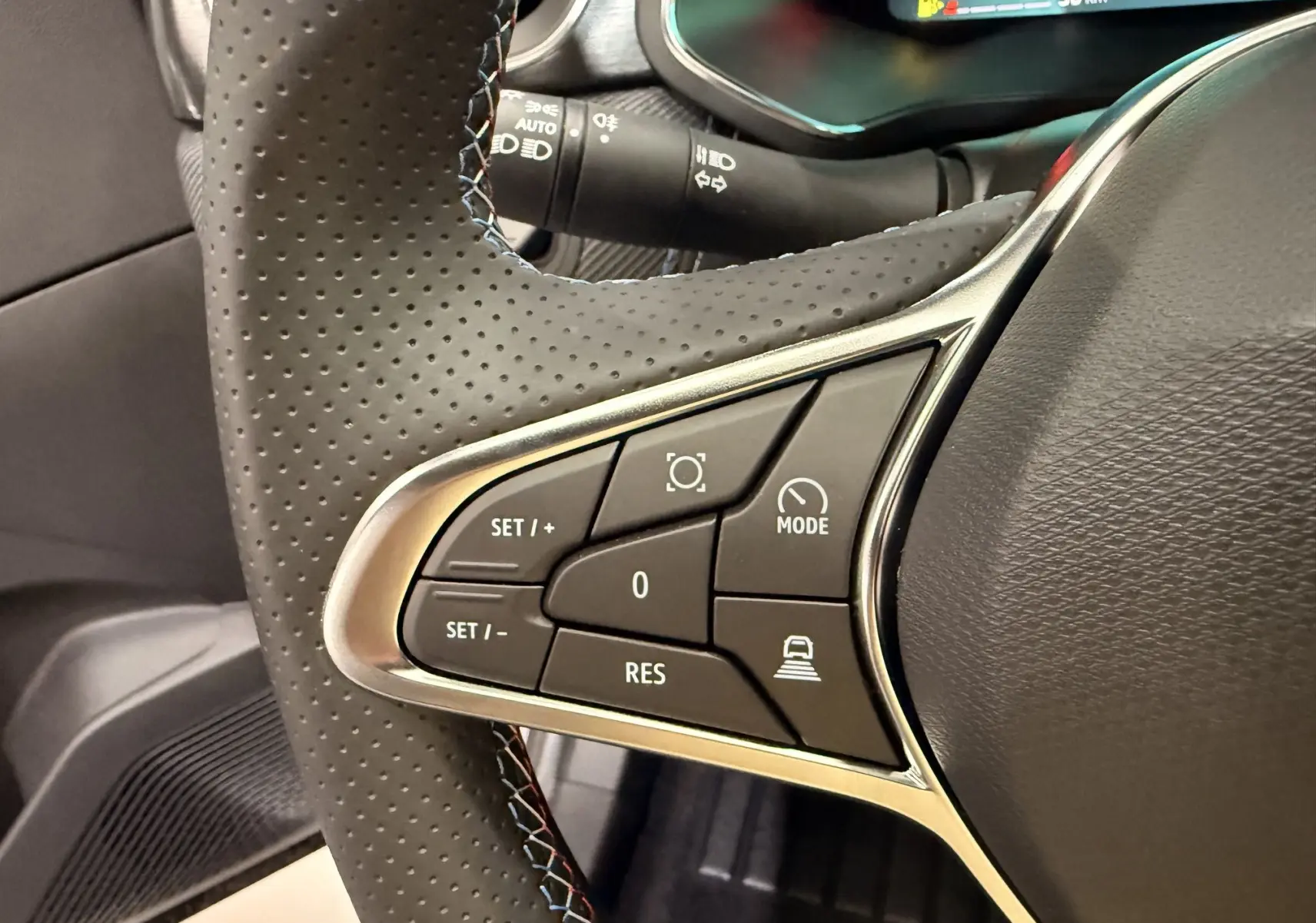 Gros plan sur les commandes gauche du volant perforé noir du Renault SYMBIOZ E-Tech 2026, avec surpiqûres tricolores.
