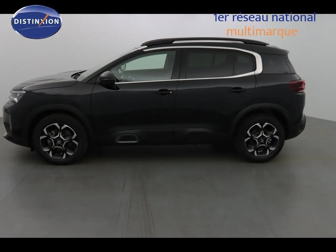 Vue 3/4 arrière d'un Citroën C5 Aircross noir métal avec jantes bi-ton et barres de toit visibles.