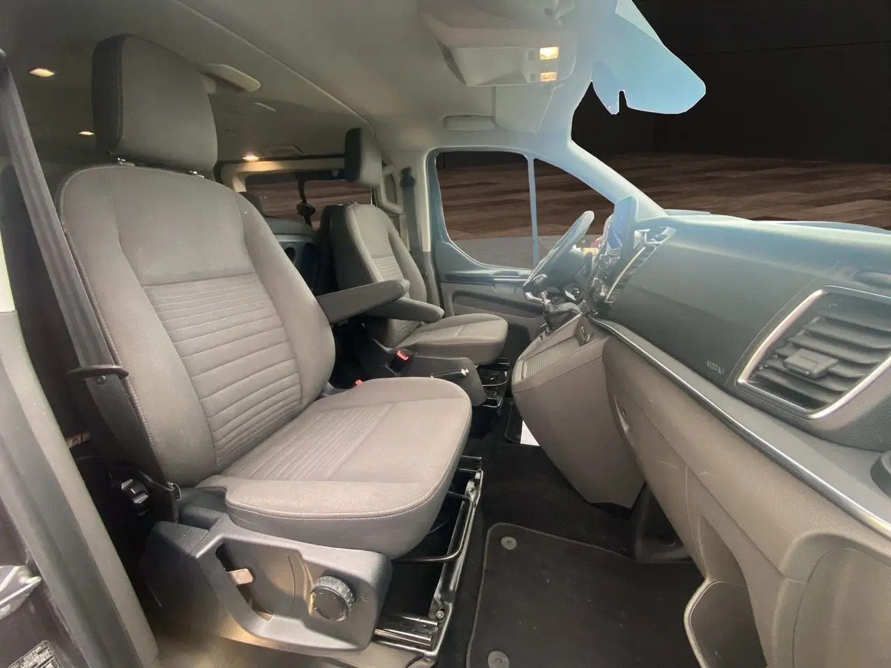 Vue intérieure côté conducteur du Ford Tourneo Custom 2020, montrant les sièges gris et le tableau de bord moderne.