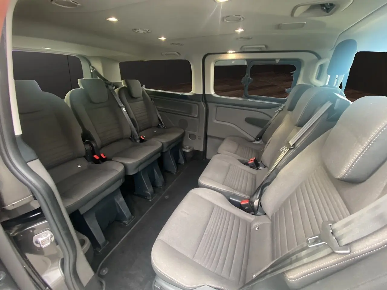 Vue intérieure du Ford Tourneo Custom 2020 montrant les sièges en tissu gris et l'aménagement spacieux pour 8 passagers.
